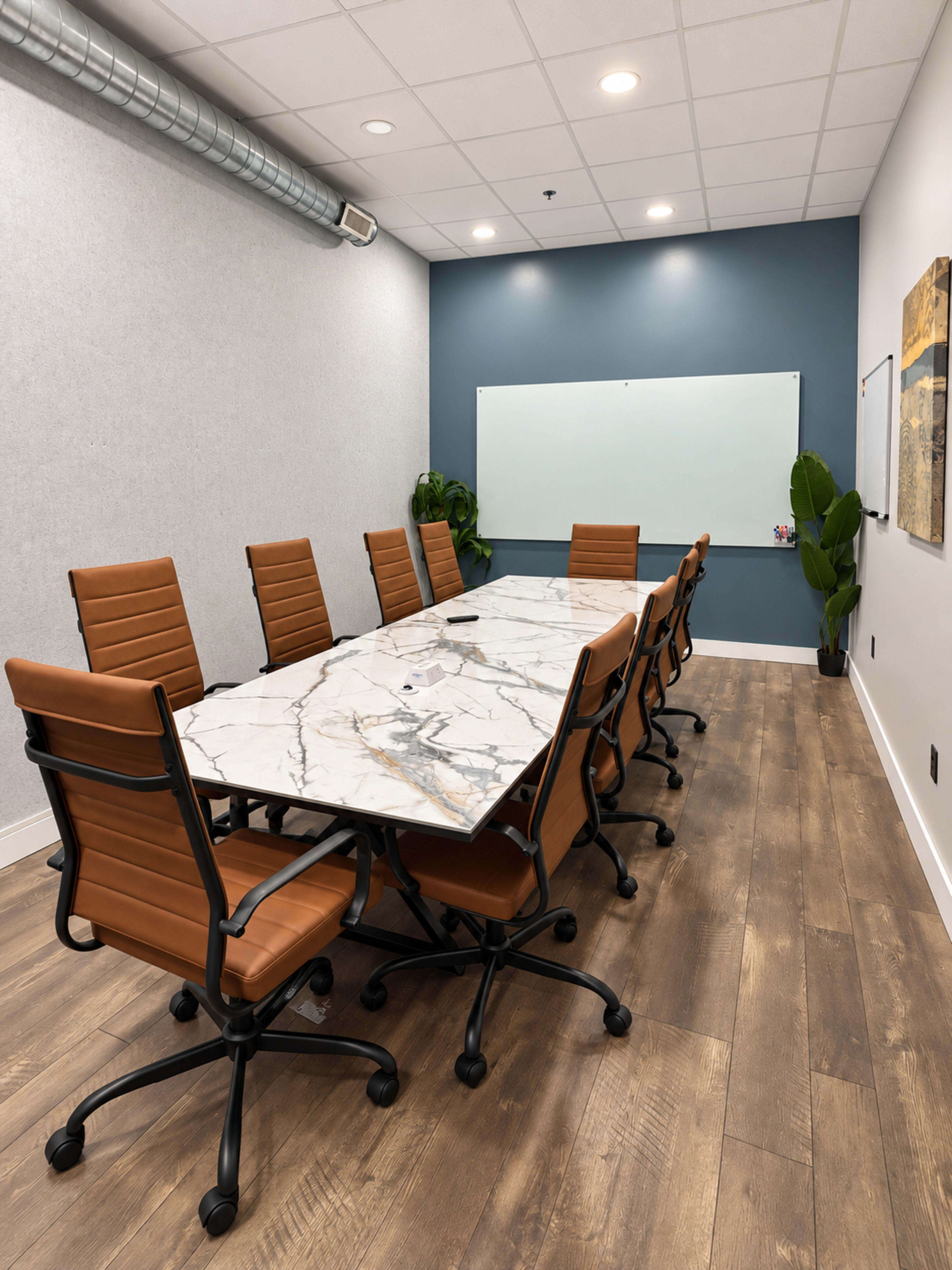 A modern conference room features a long marble table surrounded by brown leather office chairs, with a whiteboard and plant in the background.