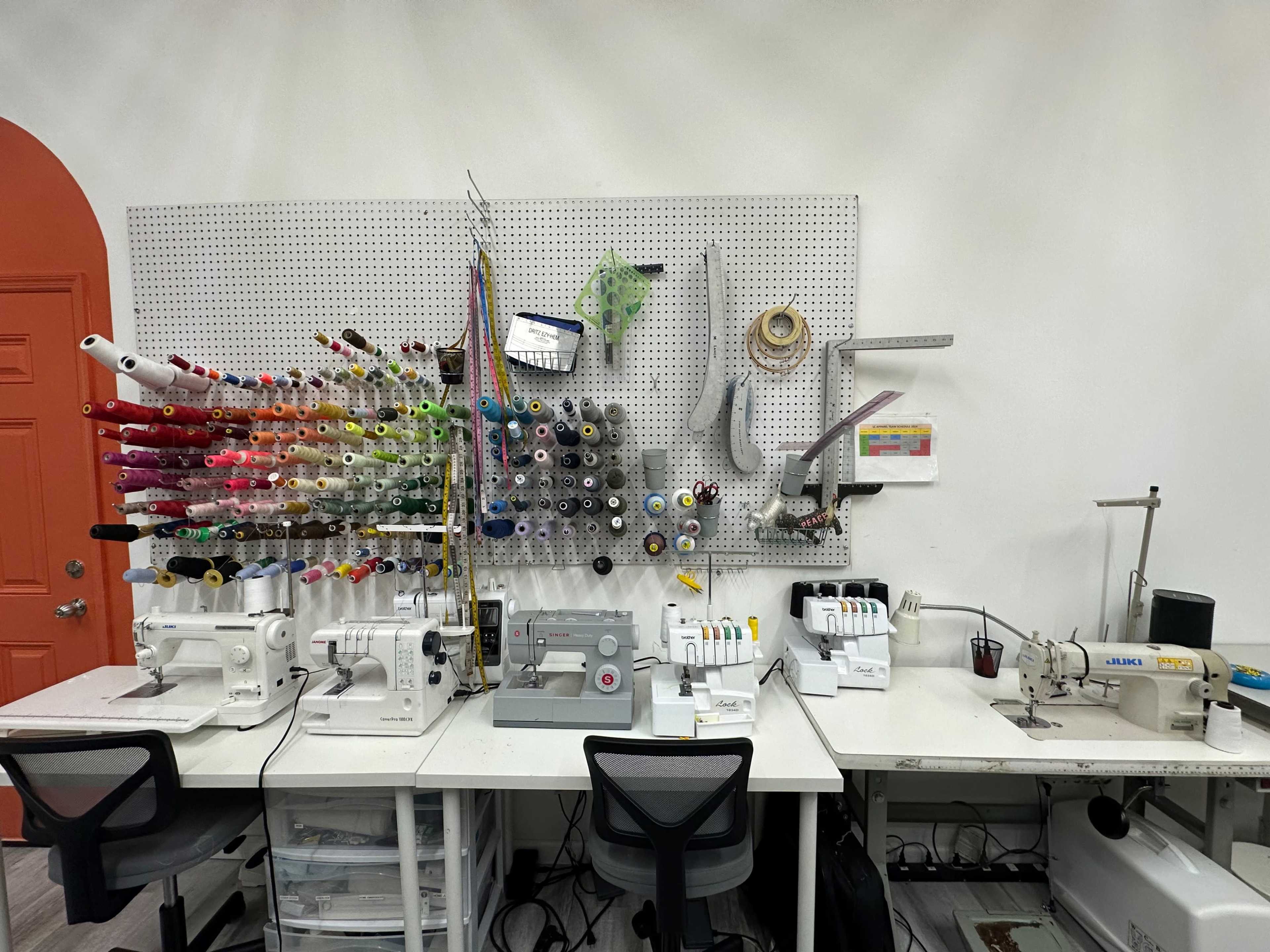 A workshop featuring multiple sewing machines and a wall organizer with colorful spools of thread.