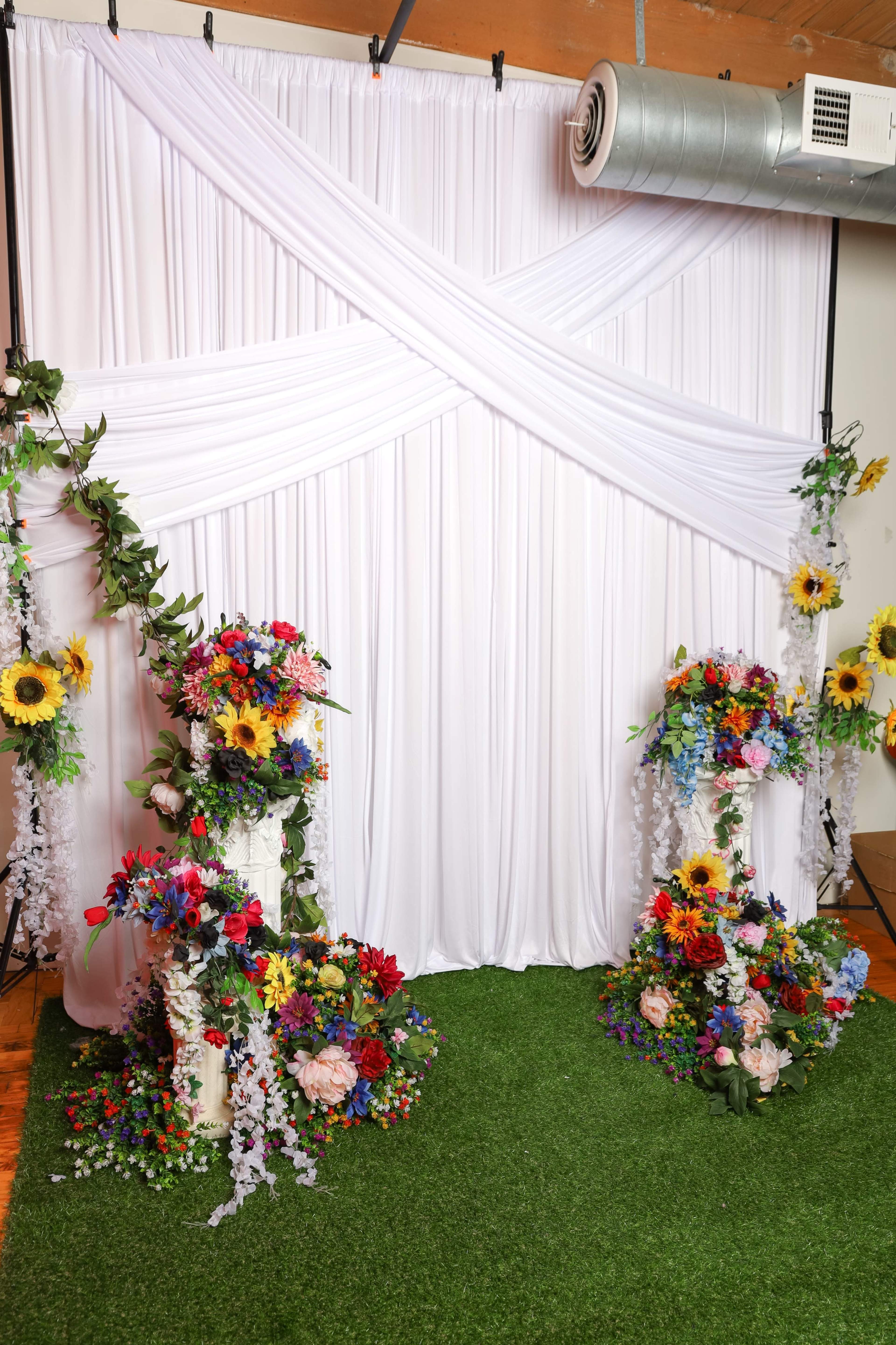 The scene features a white fabric backdrop adorned with floral arrangements on either side and a patch of green grass in front.