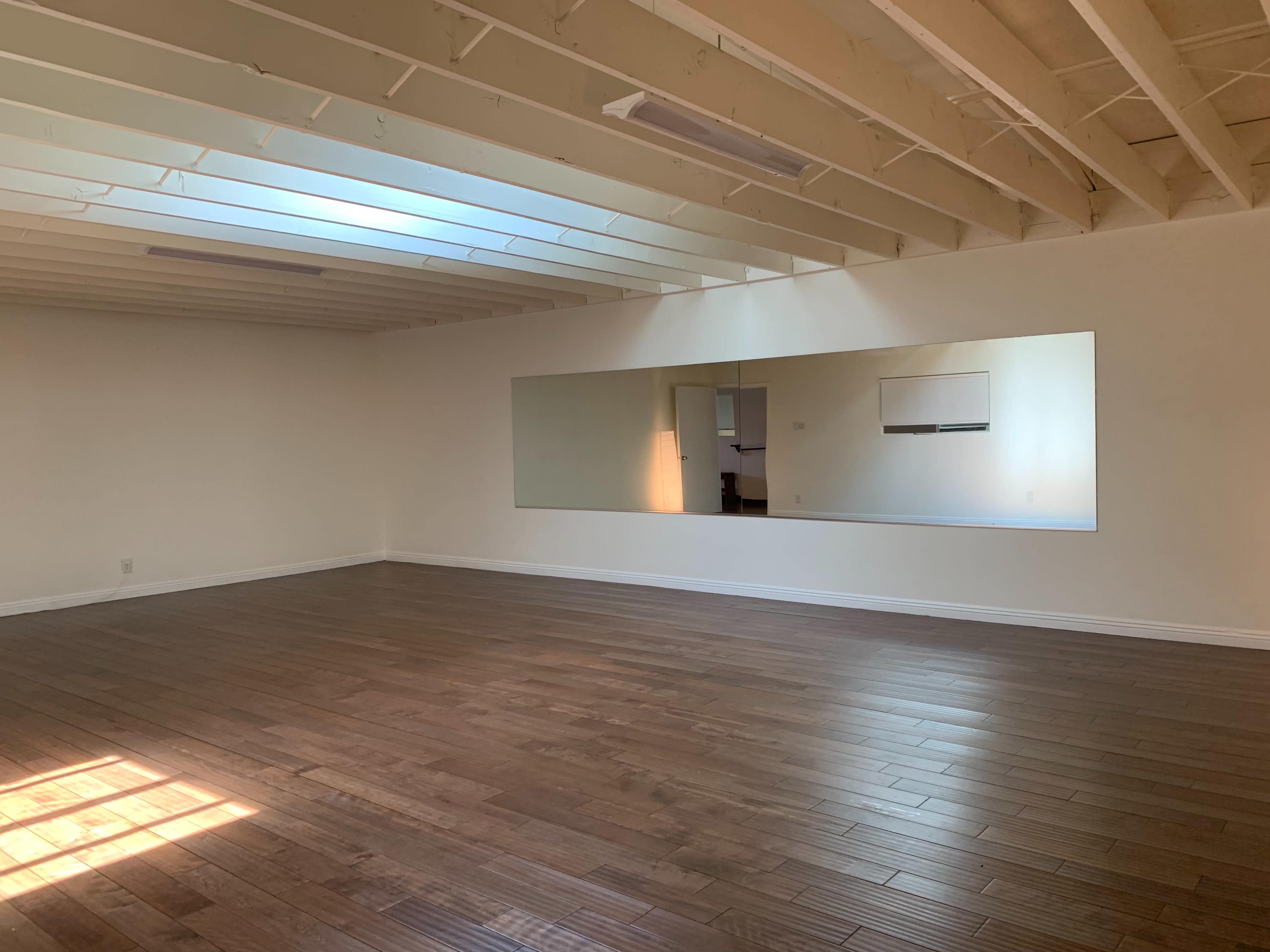 A spacious room with wooden floors, a large mirror on one wall, and natural light coming through a skylight.