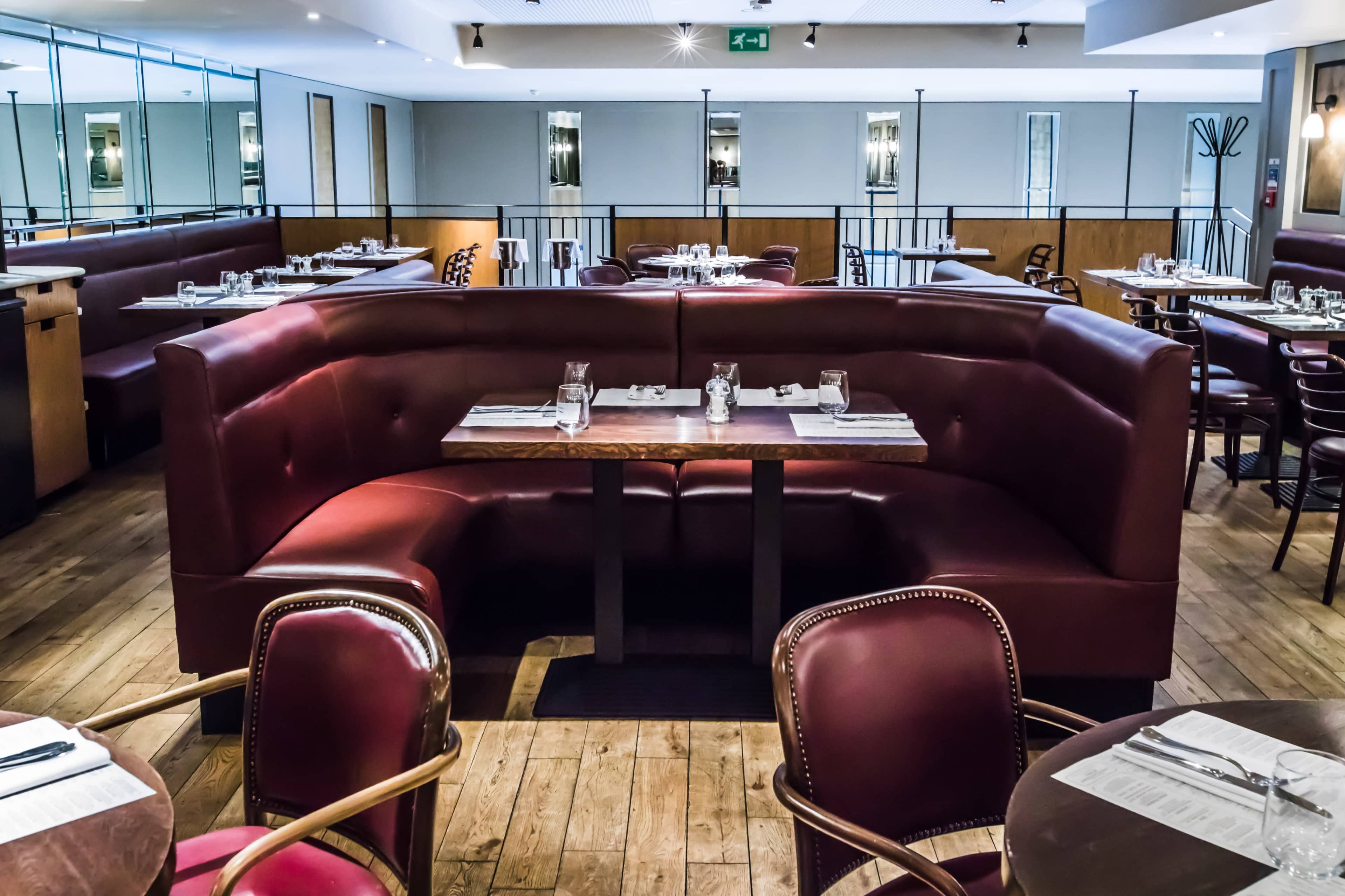 The image features a modern restaurant interior with burgundy booths, wooden flooring, and neatly arranged tables set for dining.