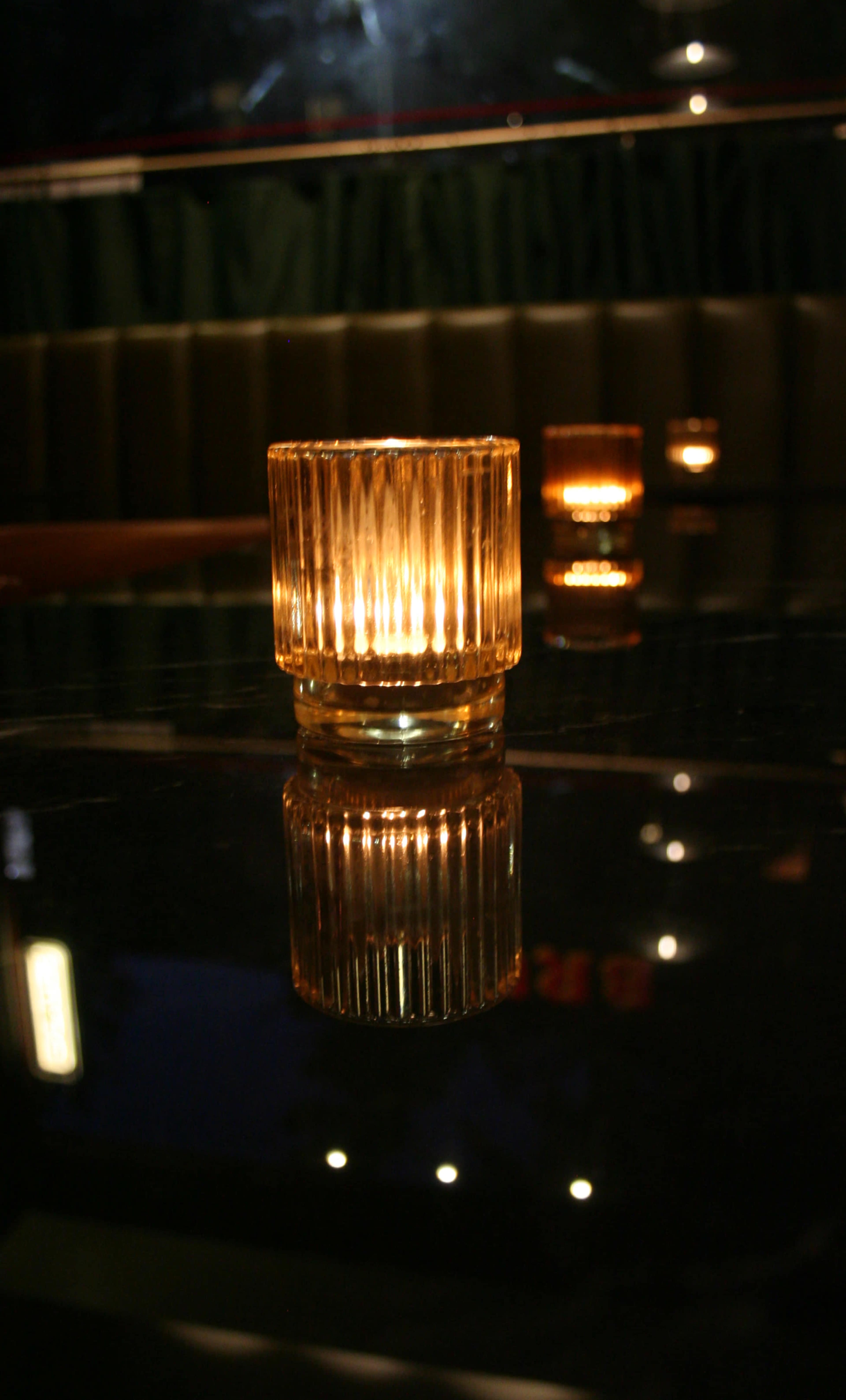 A lit decorative candle sits on a glass table, casting reflections on its surface.