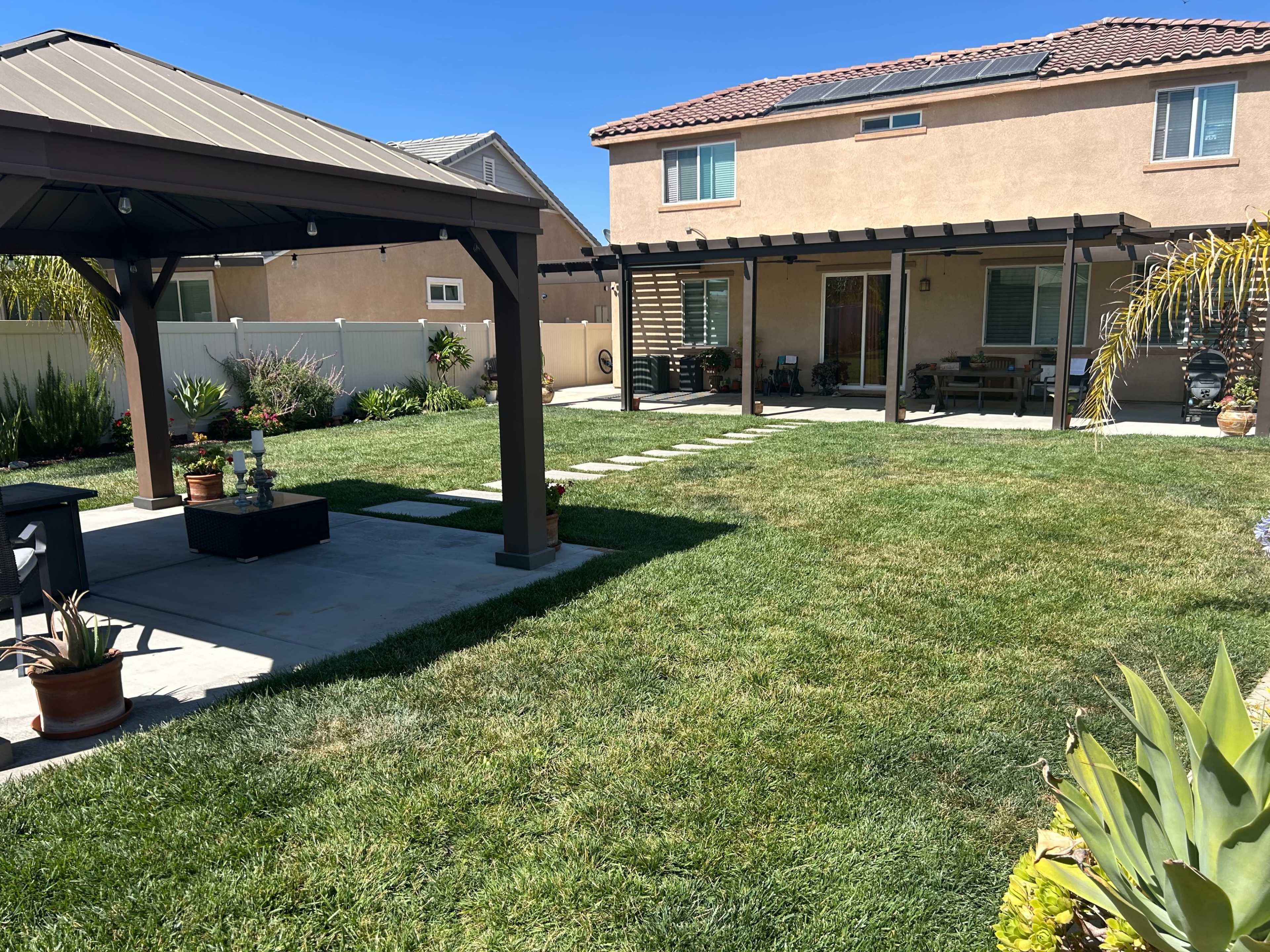 The image shows a well-maintained backyard with a grassy area, a gazebo, and a patio located behind a house.