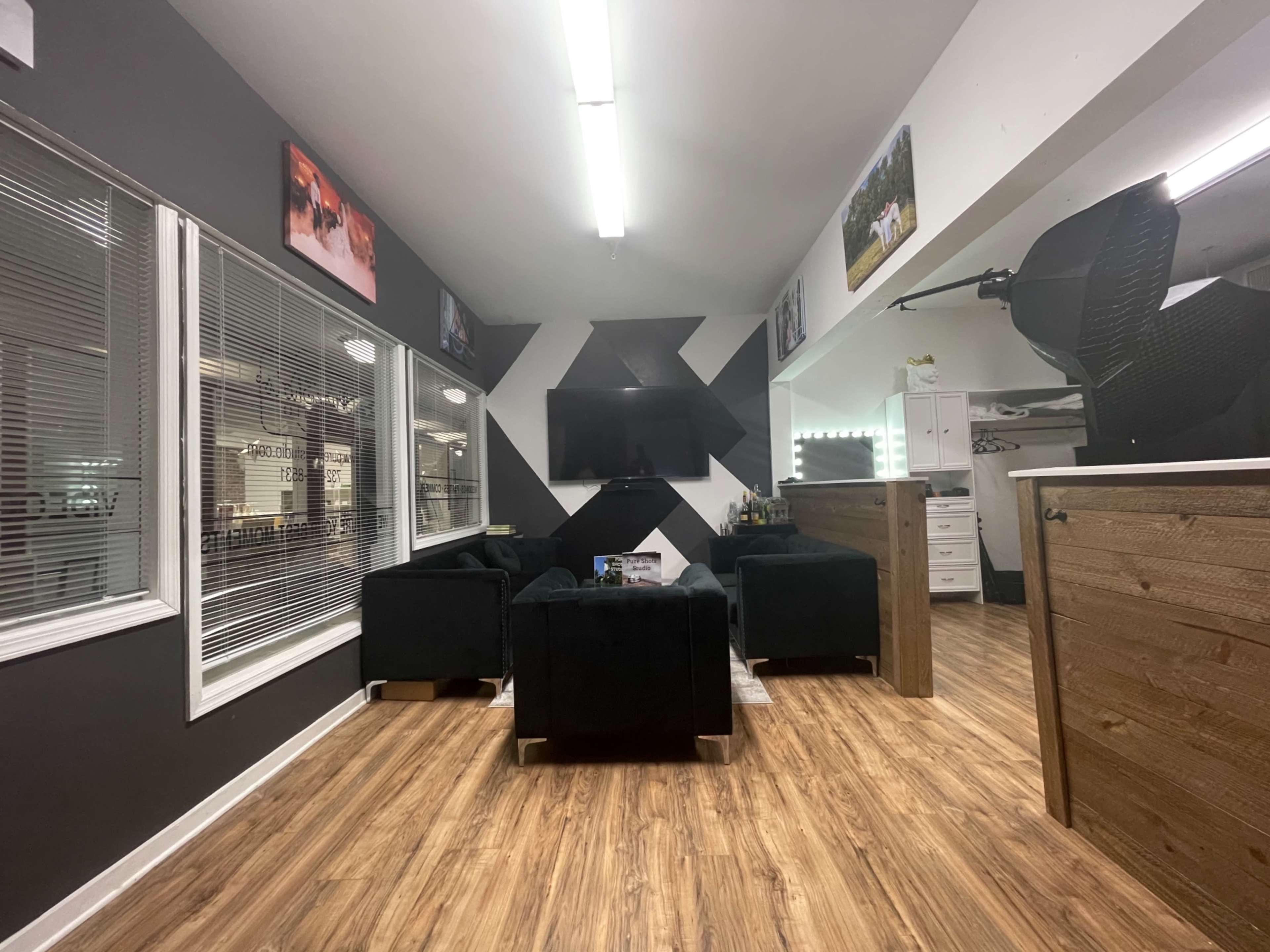 A modern lounge area with black furniture, a large wall-mounted television, and decorative wall art in a bright room with wood flooring.