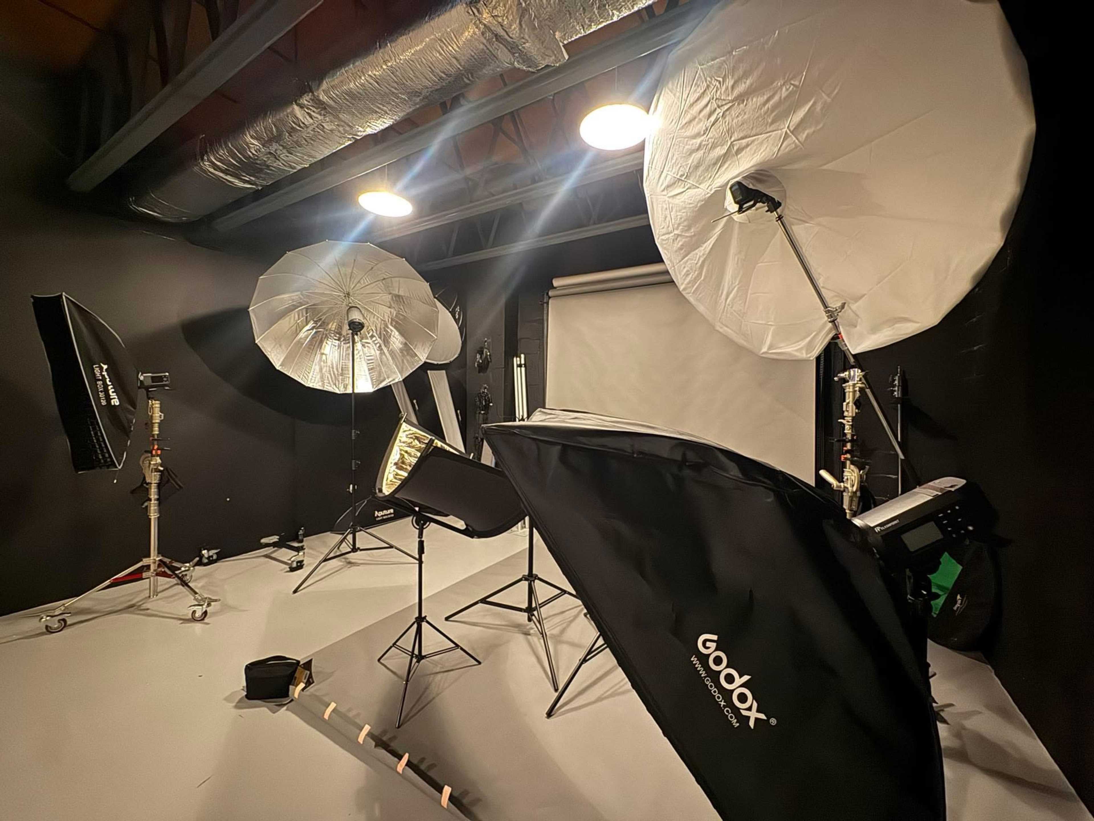 The image shows a photography studio with multiple light setups, softboxes, and a backdrop.