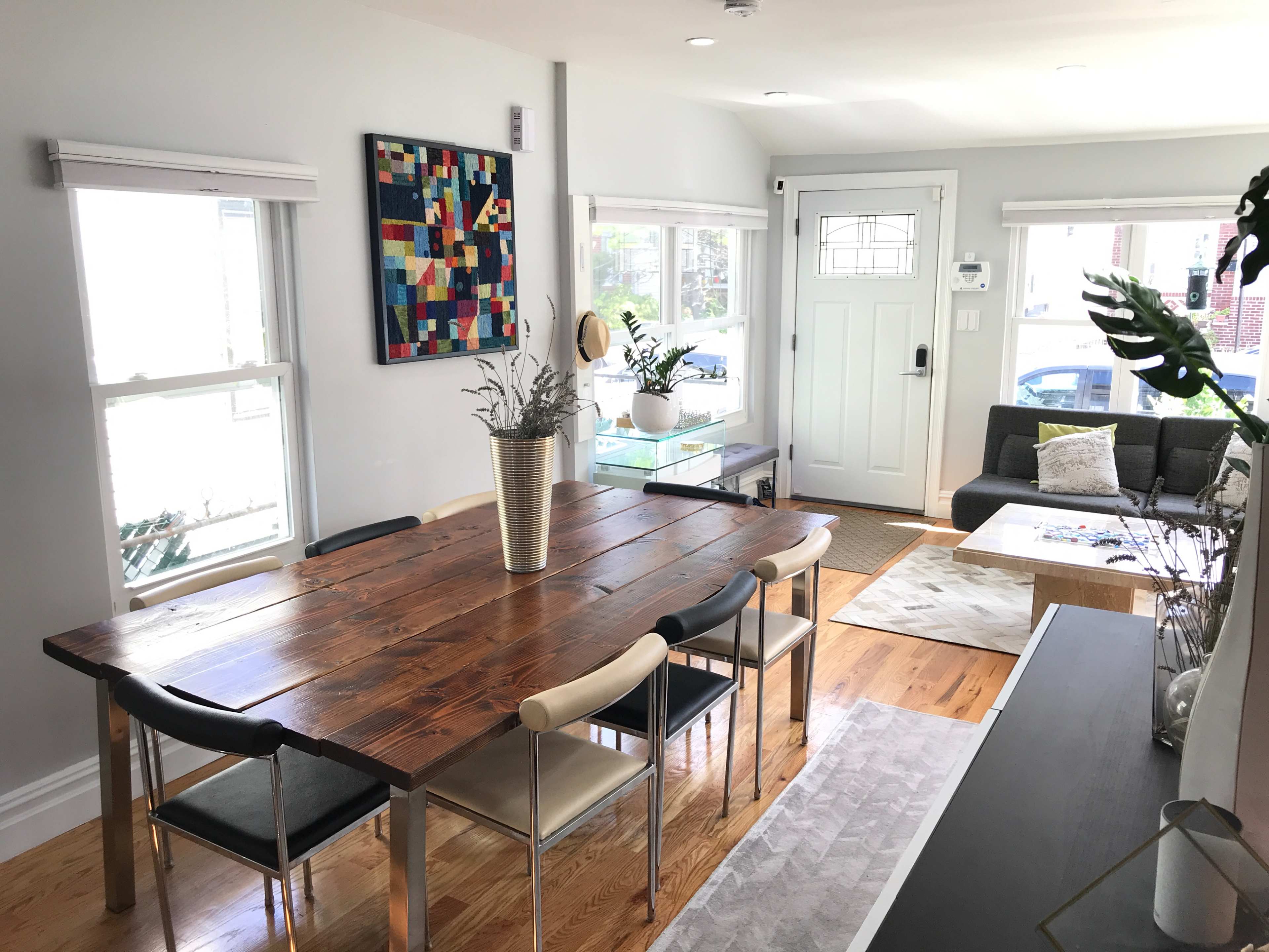 A modern dining area features a wooden table surrounded by chairs, with large windows and a door leading to an outdoor space.