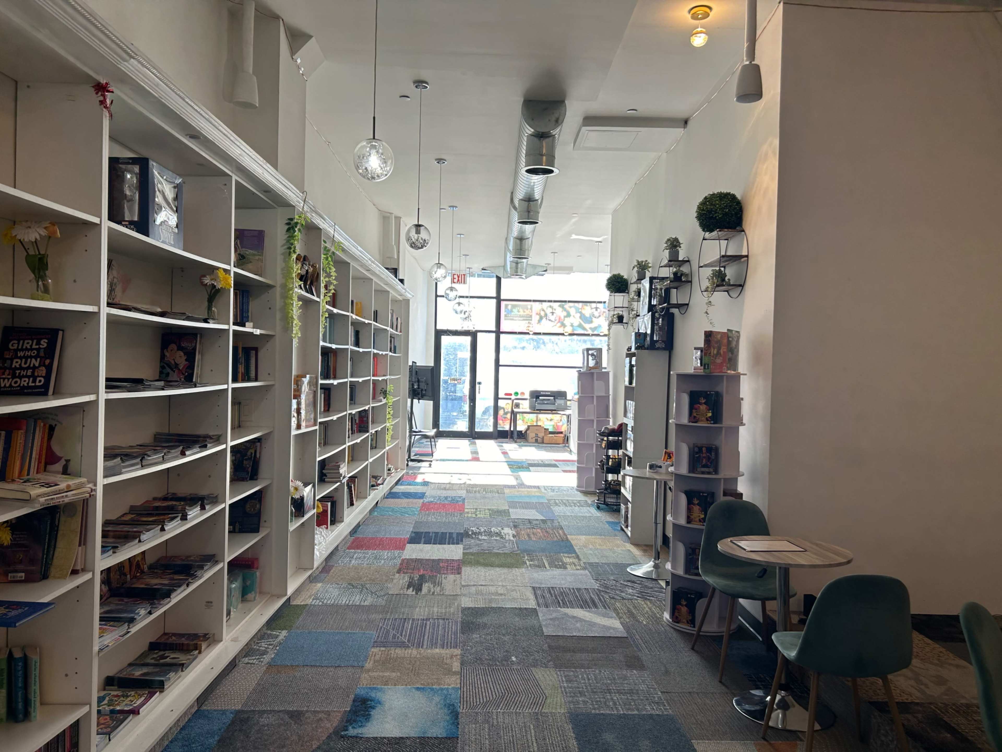 A long hallway lined with bookshelves, colorful carpet tiles, and seating areas, leading to a bright entrance.