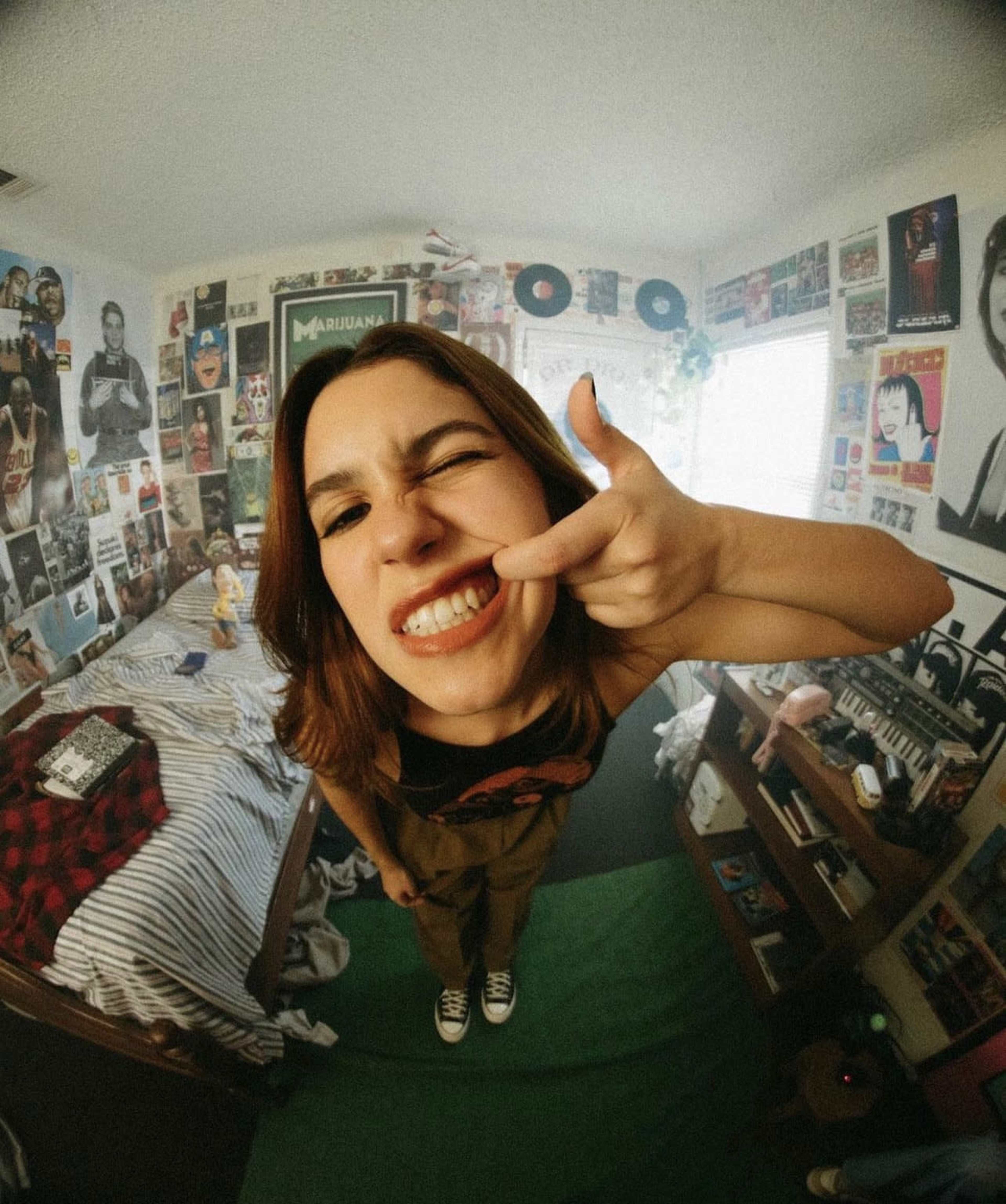 A person makes a playful gesture with their hand in a bedroom filled with music posters and various decorations.