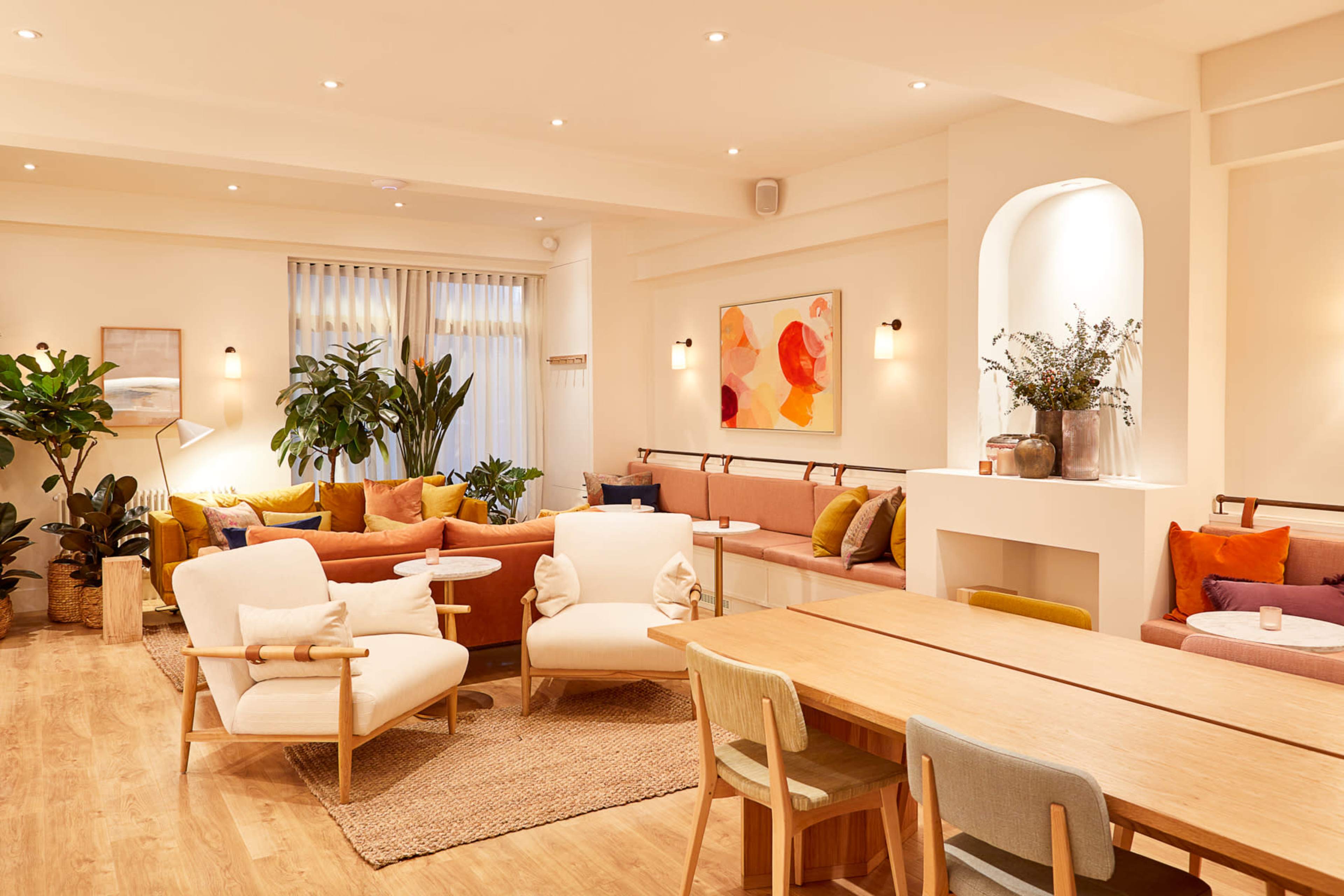 A modern, brightly lit lounge area with comfortable seating, indoor plants, and a wooden dining table.