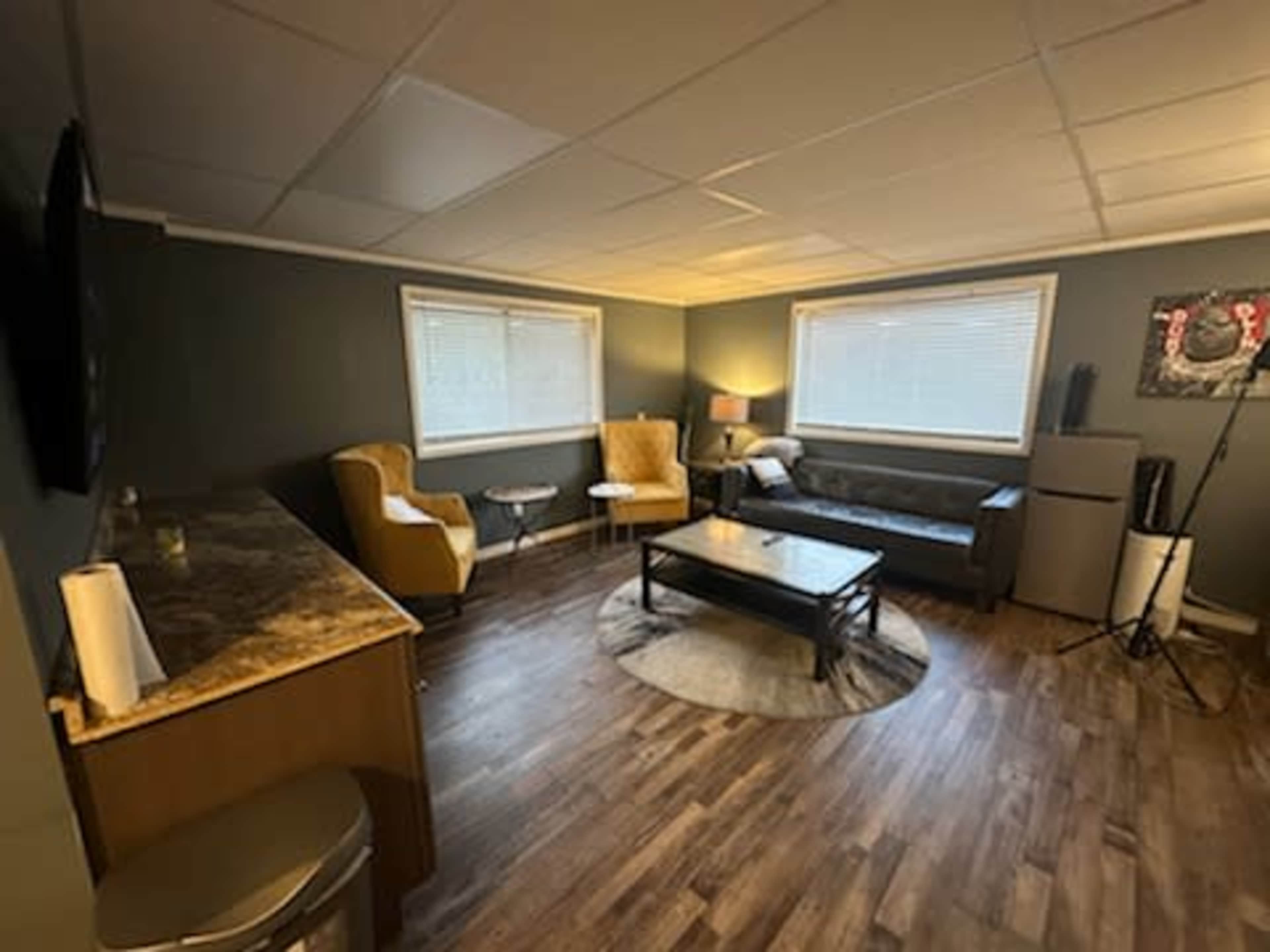 A cozy living area with a dark sofa, a small coffee table, two armchairs, and a kitchenette area against one wall.