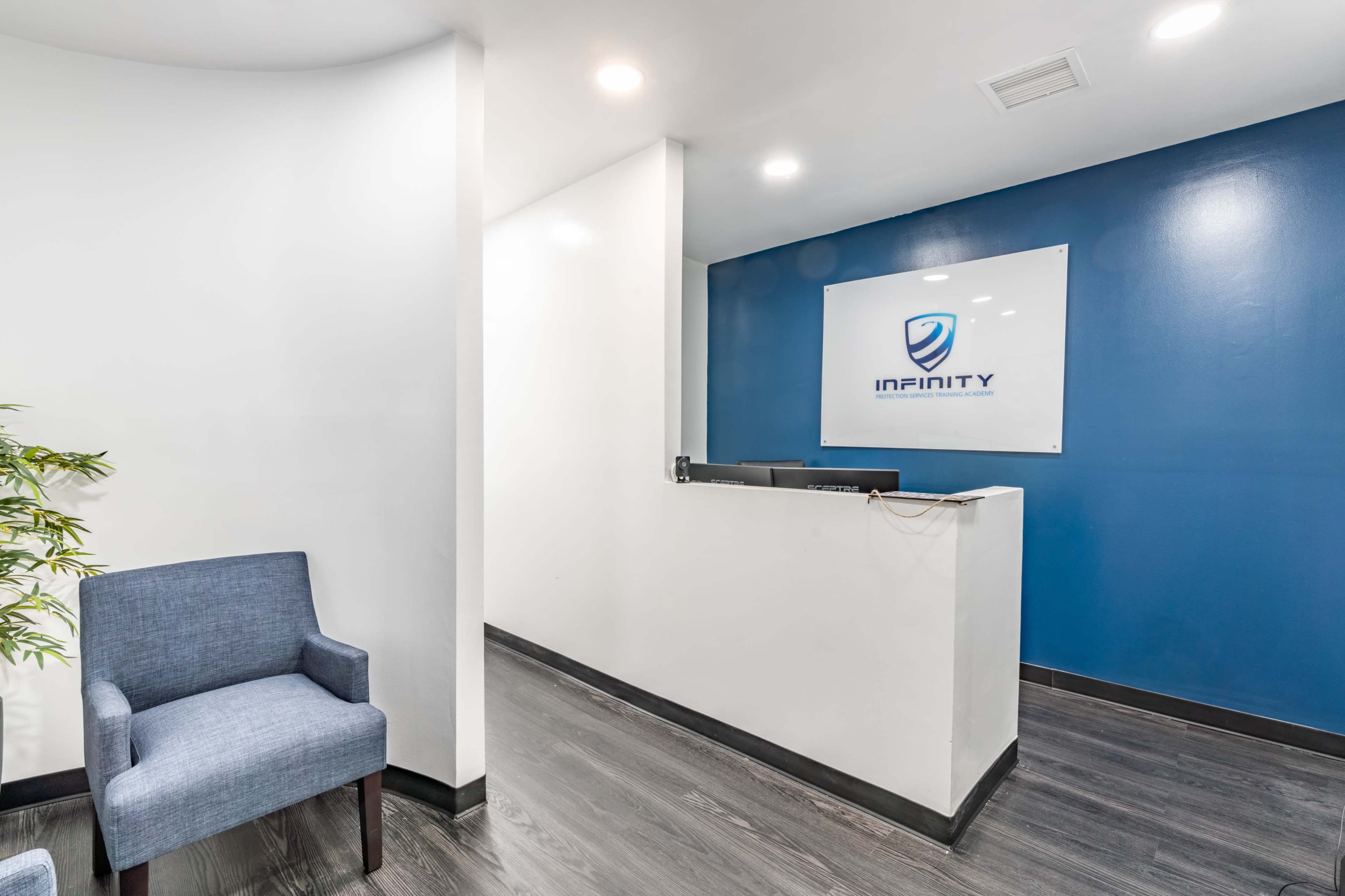 The image shows a modern reception area with a blue accent wall, a reception desk bearing the "Infinity" logo, and two blue chairs nearby.