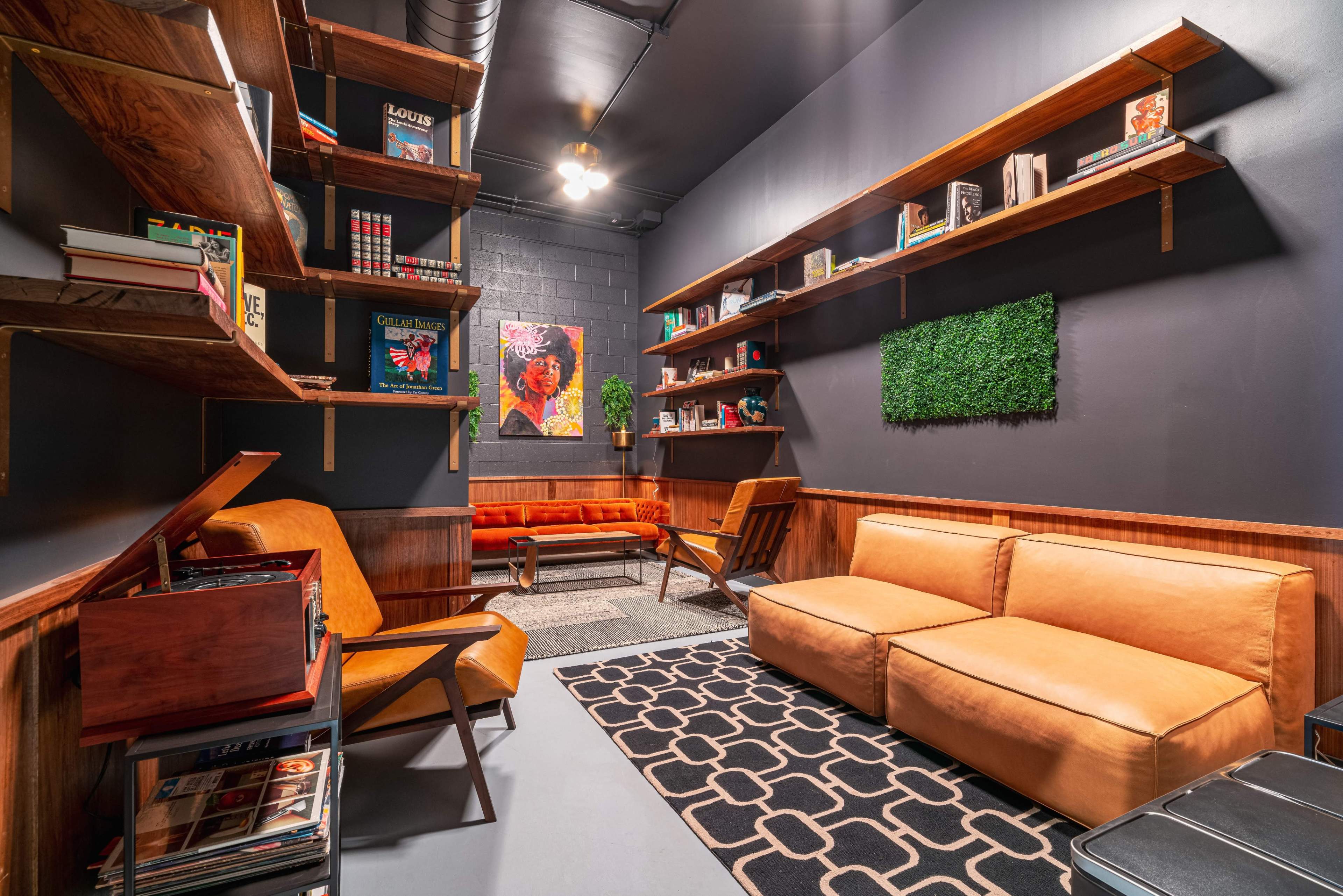 A cozy interior space featuring a modern seating arrangement, wooden shelves filled with books, and decorative elements including a green wall panel and artwork.