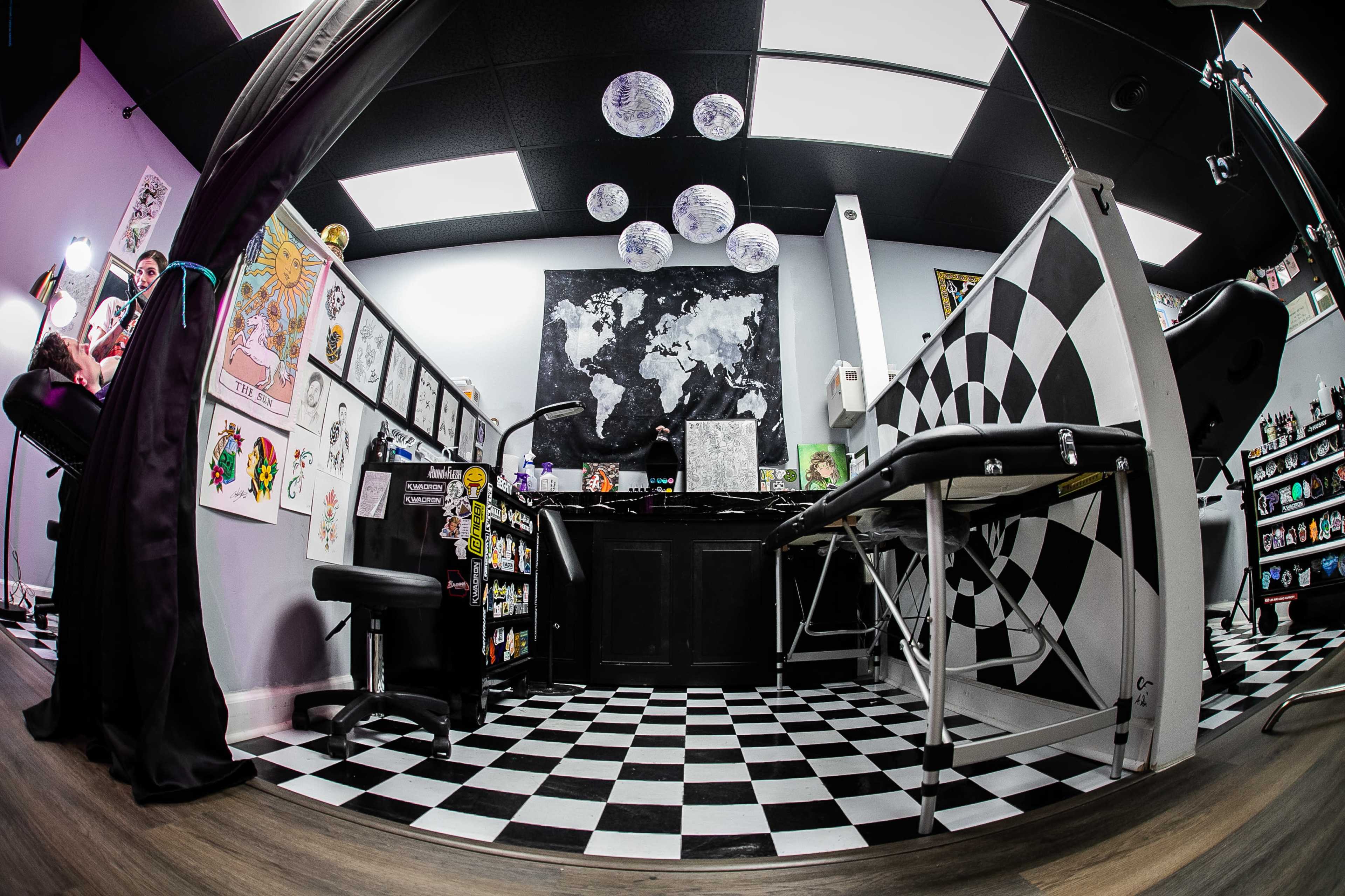 The image displays an interior view of a tattoo shop, featuring a checkered floor, wall art, and tattoo station.
