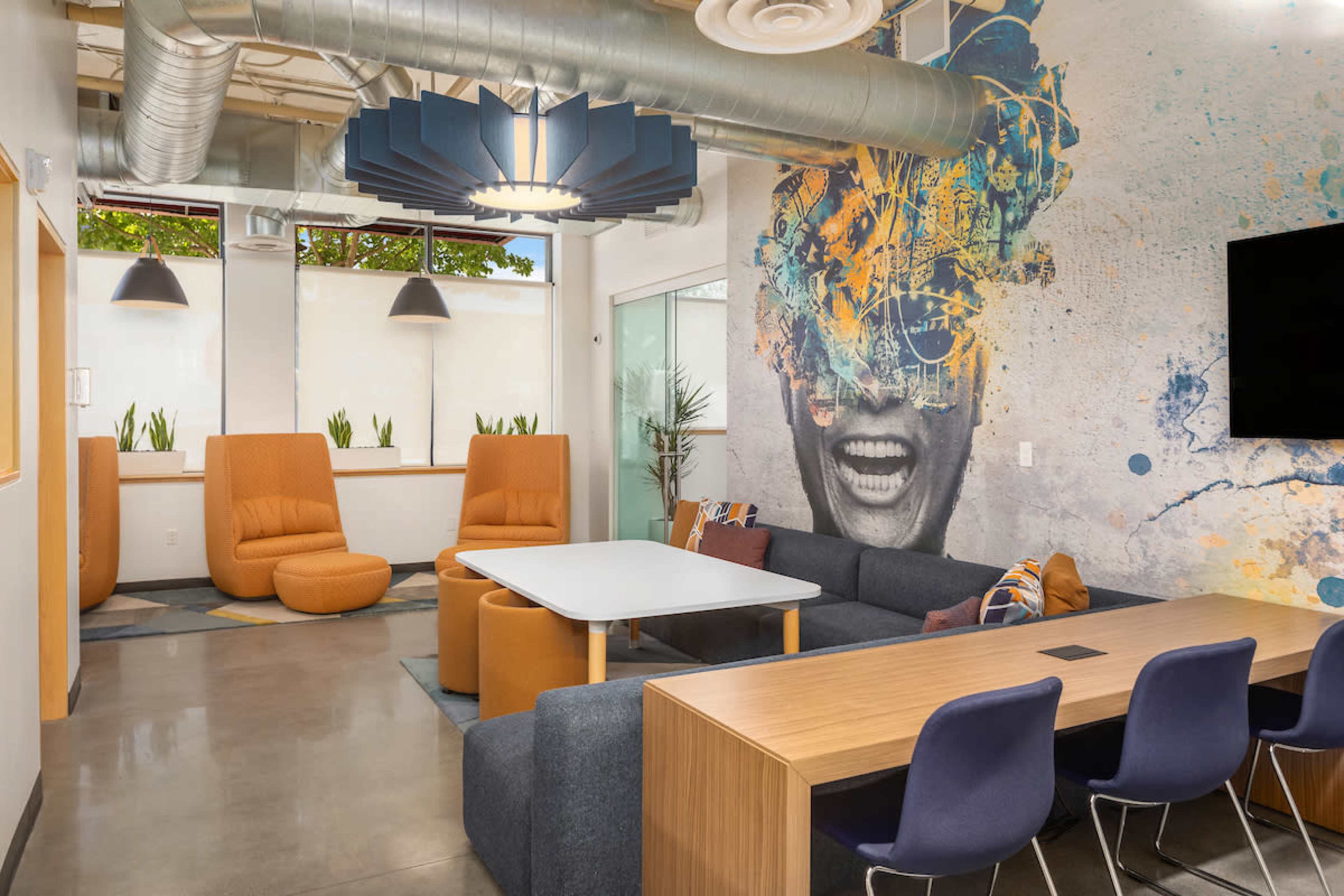 A modern lounge area featuring a large sofa, colorful chairs, a table, and a vibrant mural on the wall.
