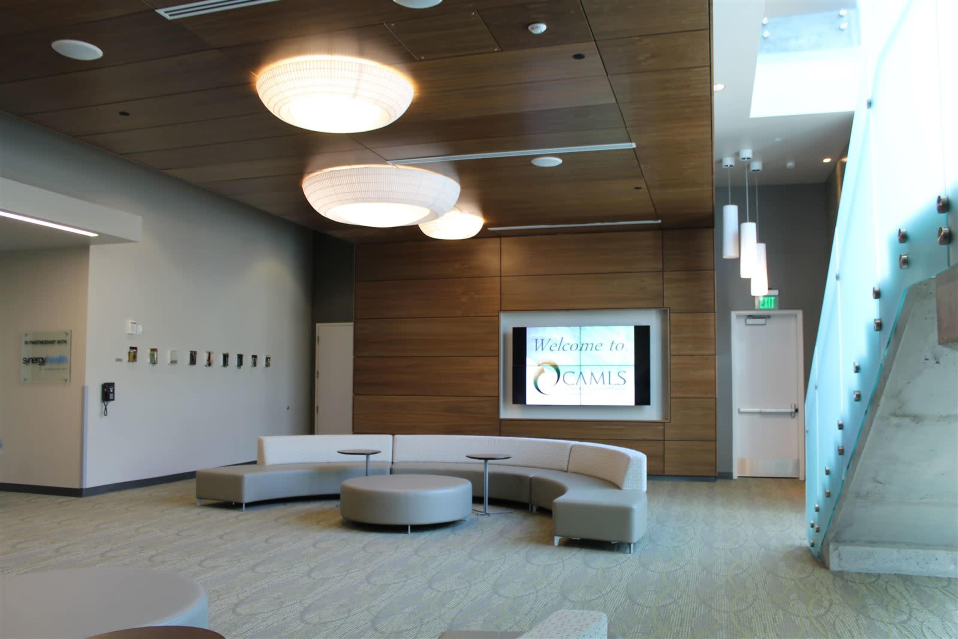 A modern lobby with curved seating arrangements and a large screen displaying "Welcome to OCAMLS" on a wooden accent wall.