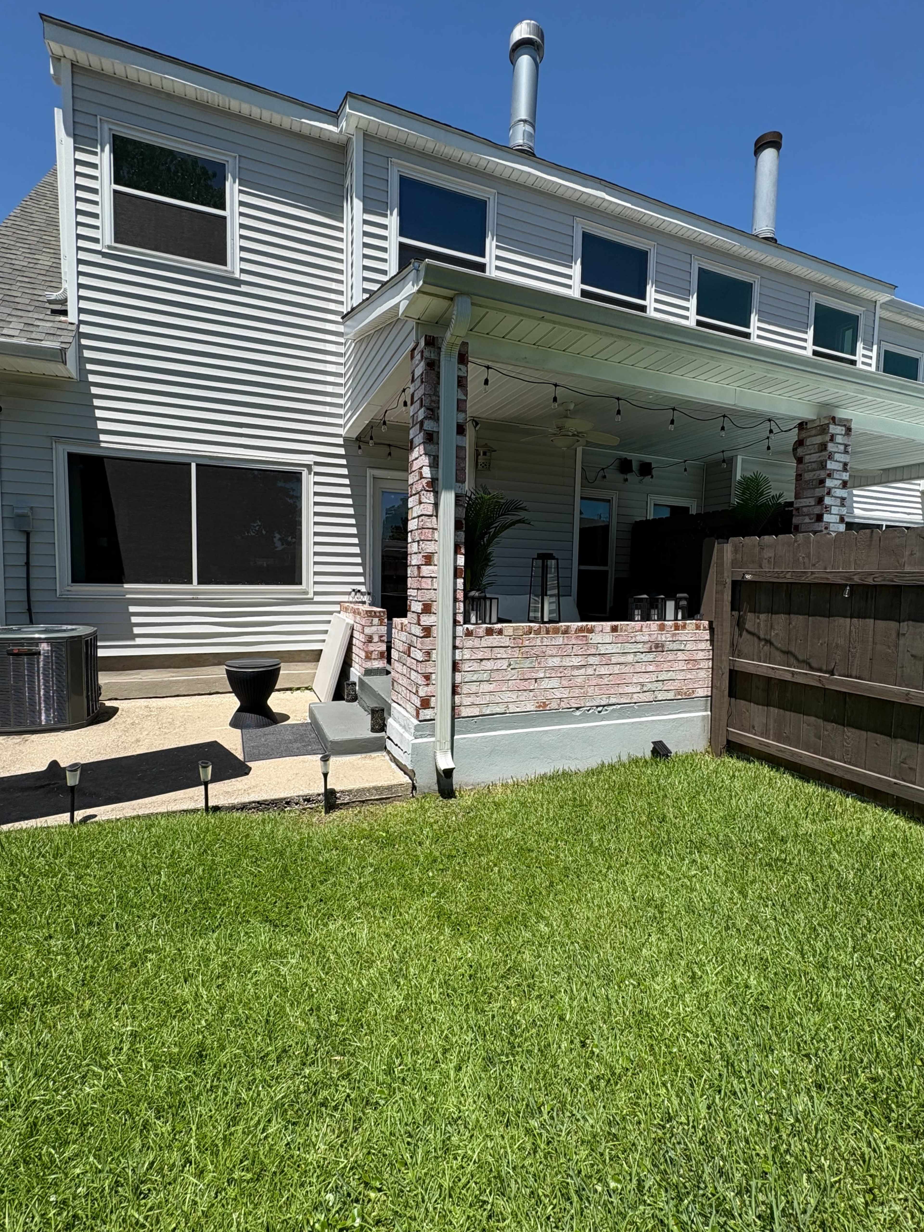 The image shows a two-story house with a spacious backyard featuring well-maintained grass, a patio area, and a wooden fence.