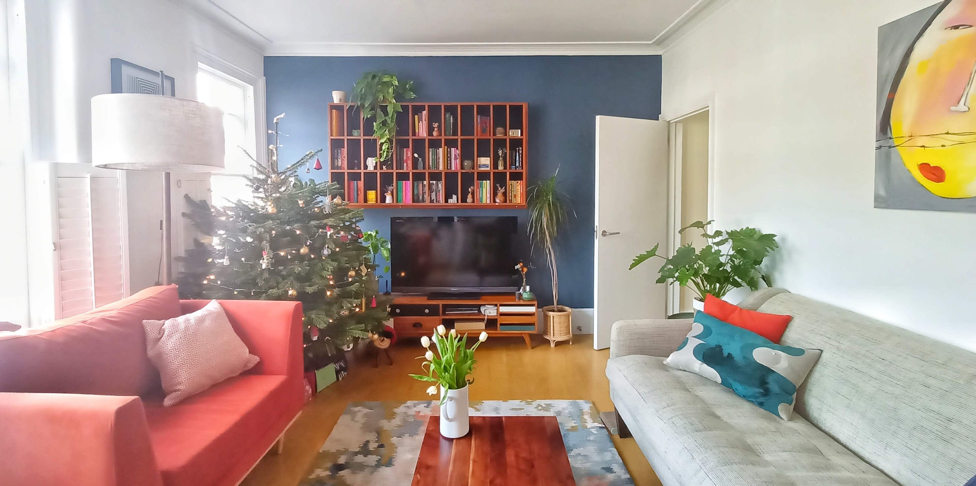 A living room with a Christmas tree, a television on a wooden stand, two sofas, and a coffee table with a vase of flowers.