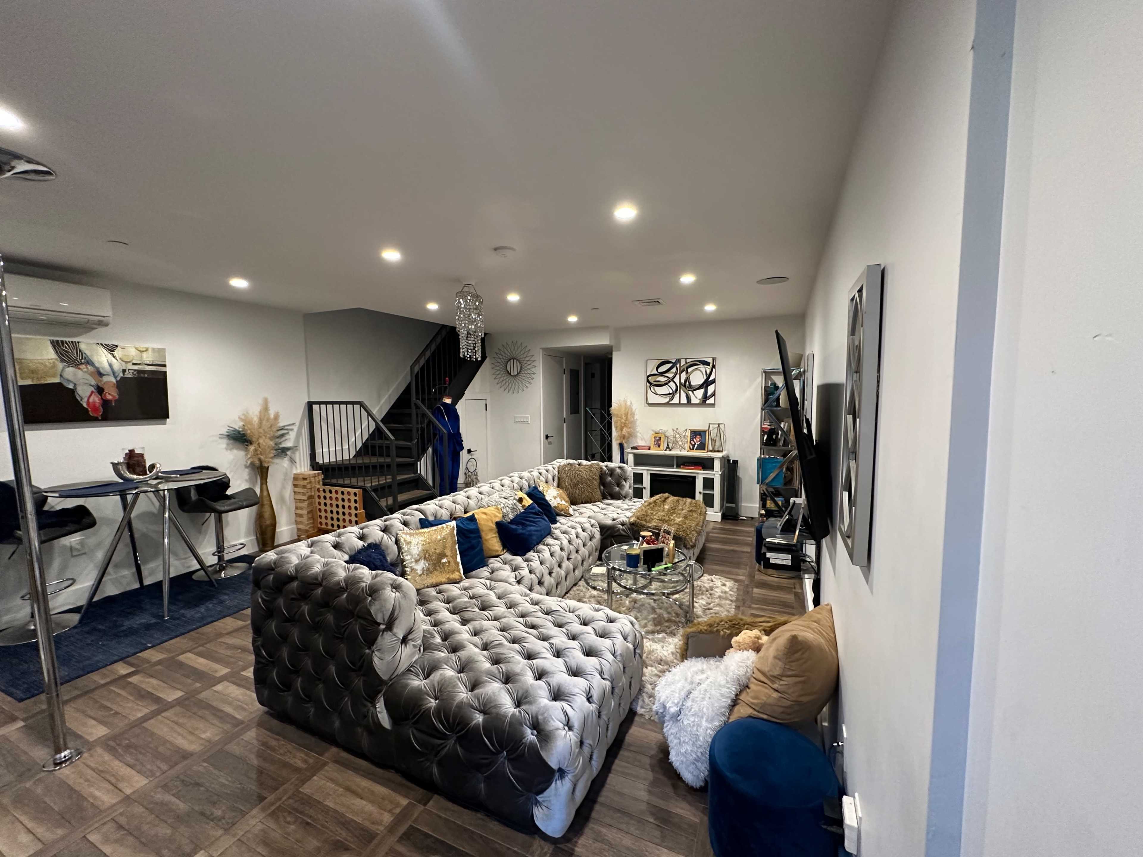 A modern living room with a large tufted sectional sofa, a coffee table, and decorative accents, alongside a staircase leading to another level.