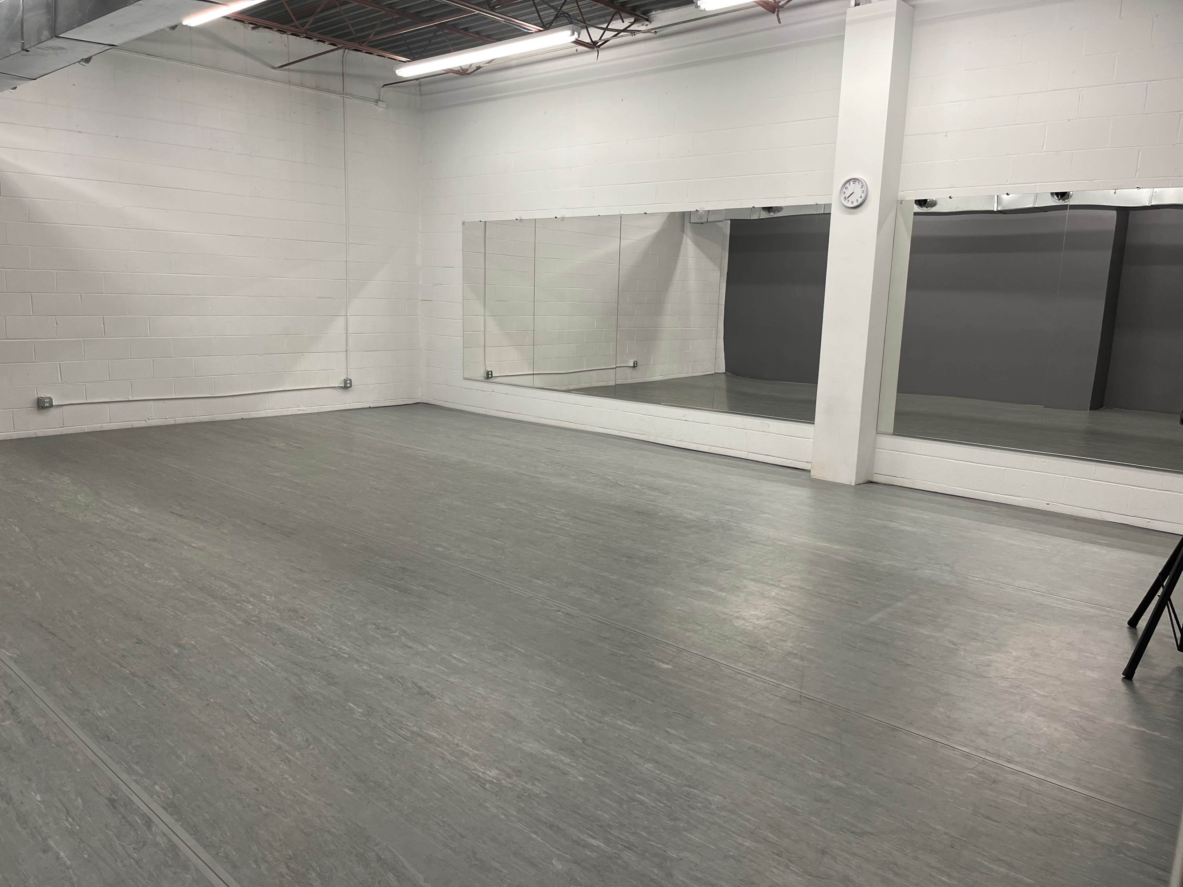 An empty room with gray flooring, white walls, and large mirrors on one side.