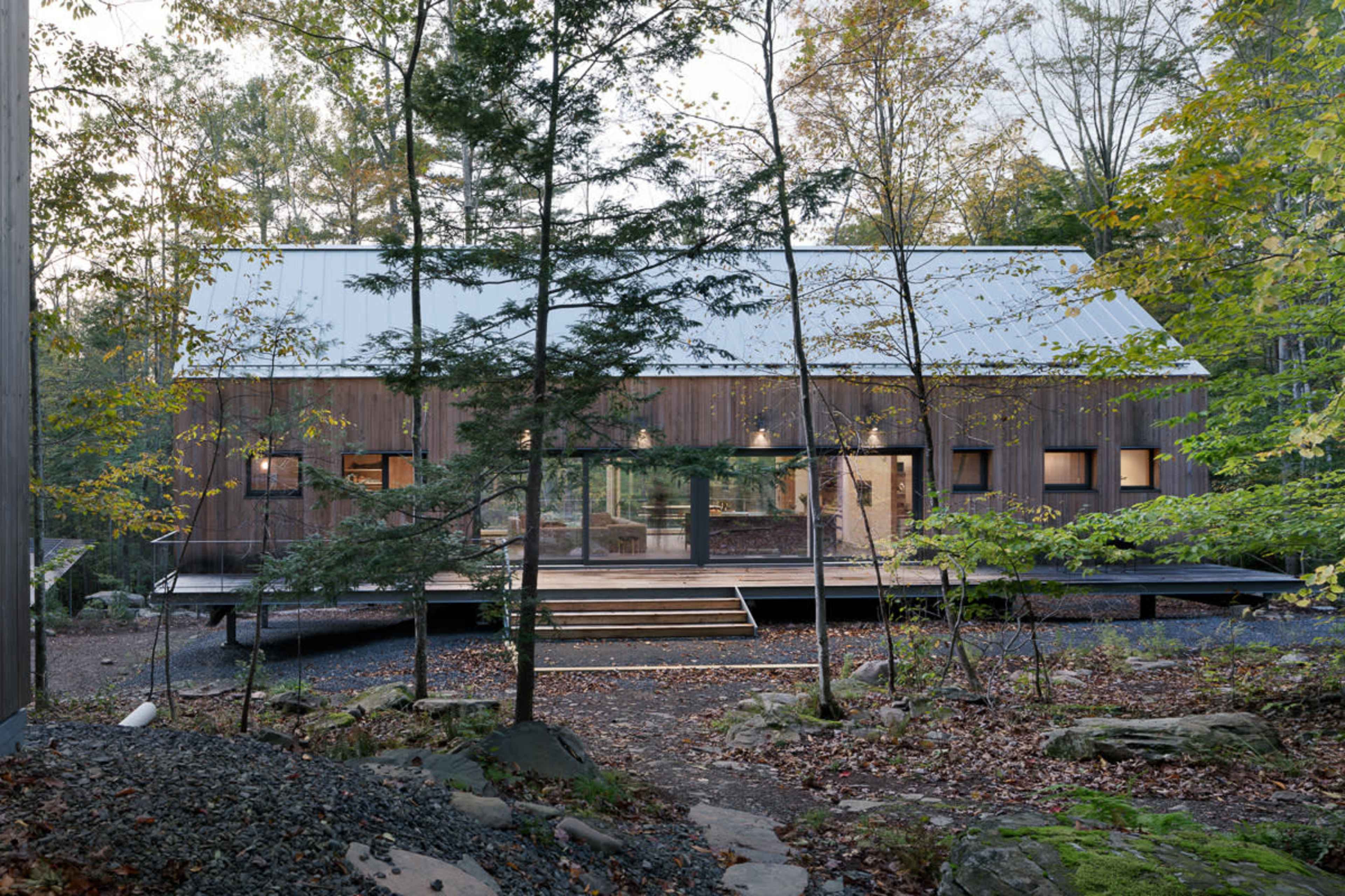 A modern wooden cabin with a metal roof is surrounded by trees and built on a raised platform in a forested area.