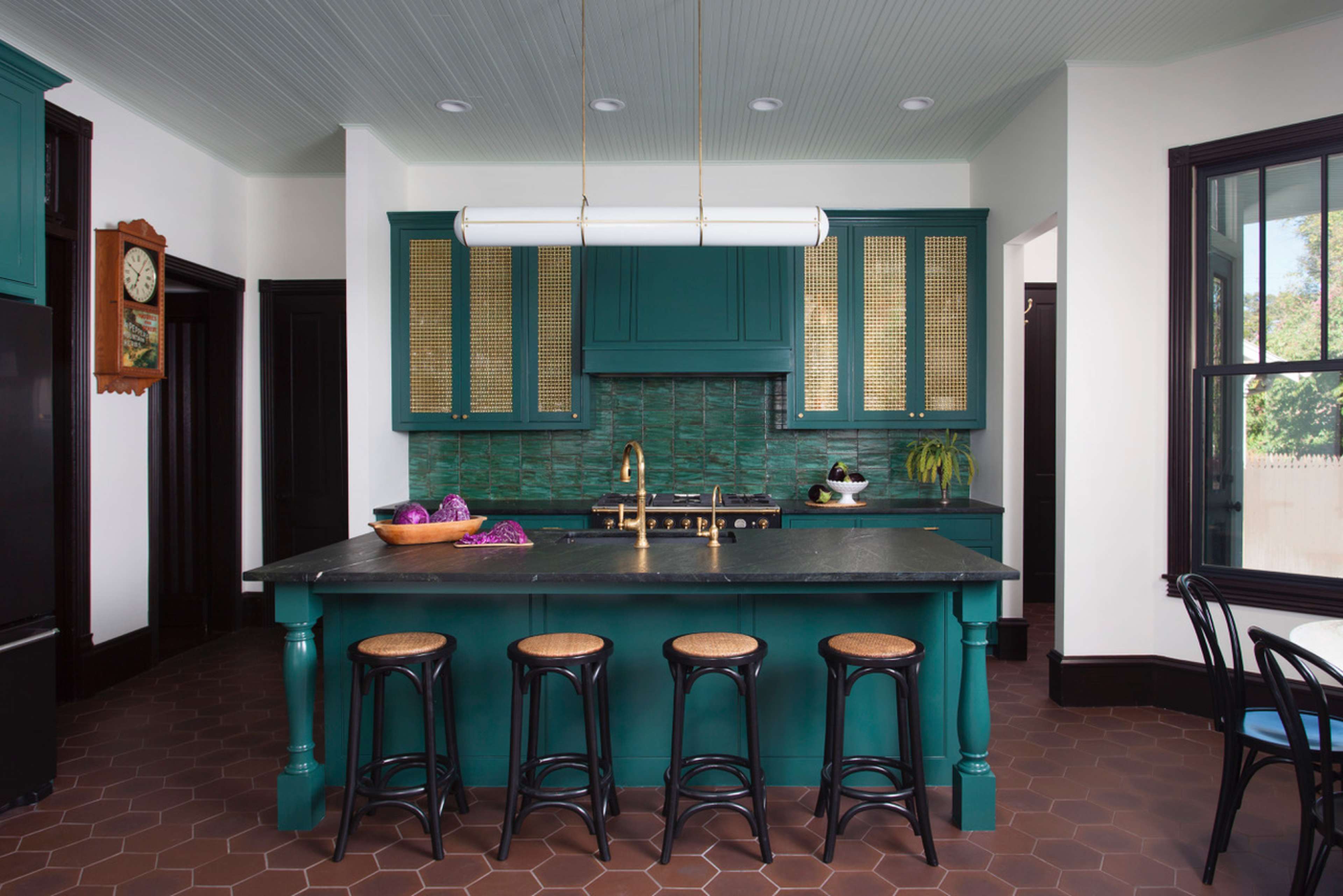 The kitchen features a large teal island with four black stools, a brass faucet, and green tile backsplash, surrounded by white walls and dark trim.