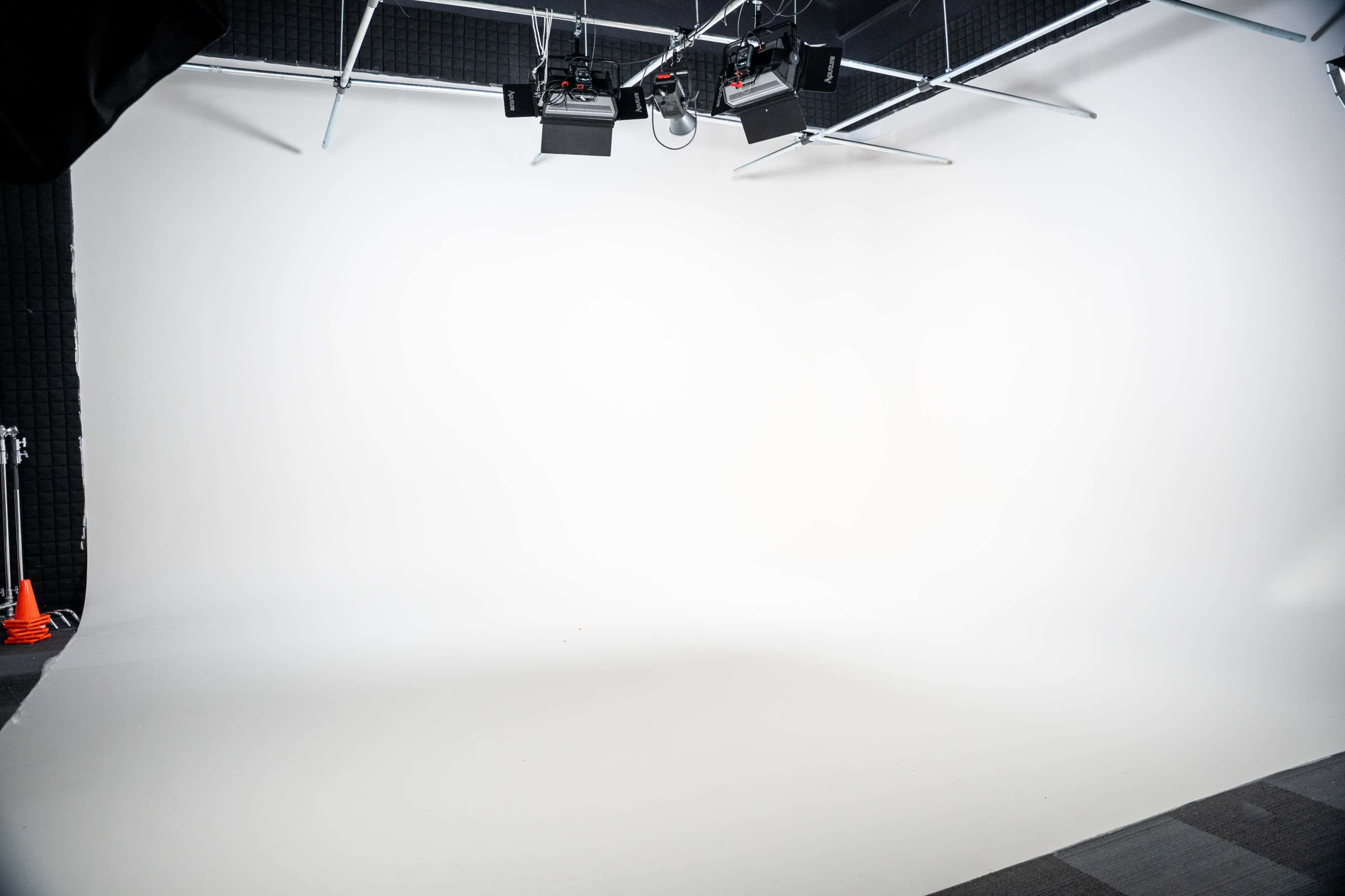 The image shows a spacious photography studio with a seamless white backdrop and overhead lighting setup.