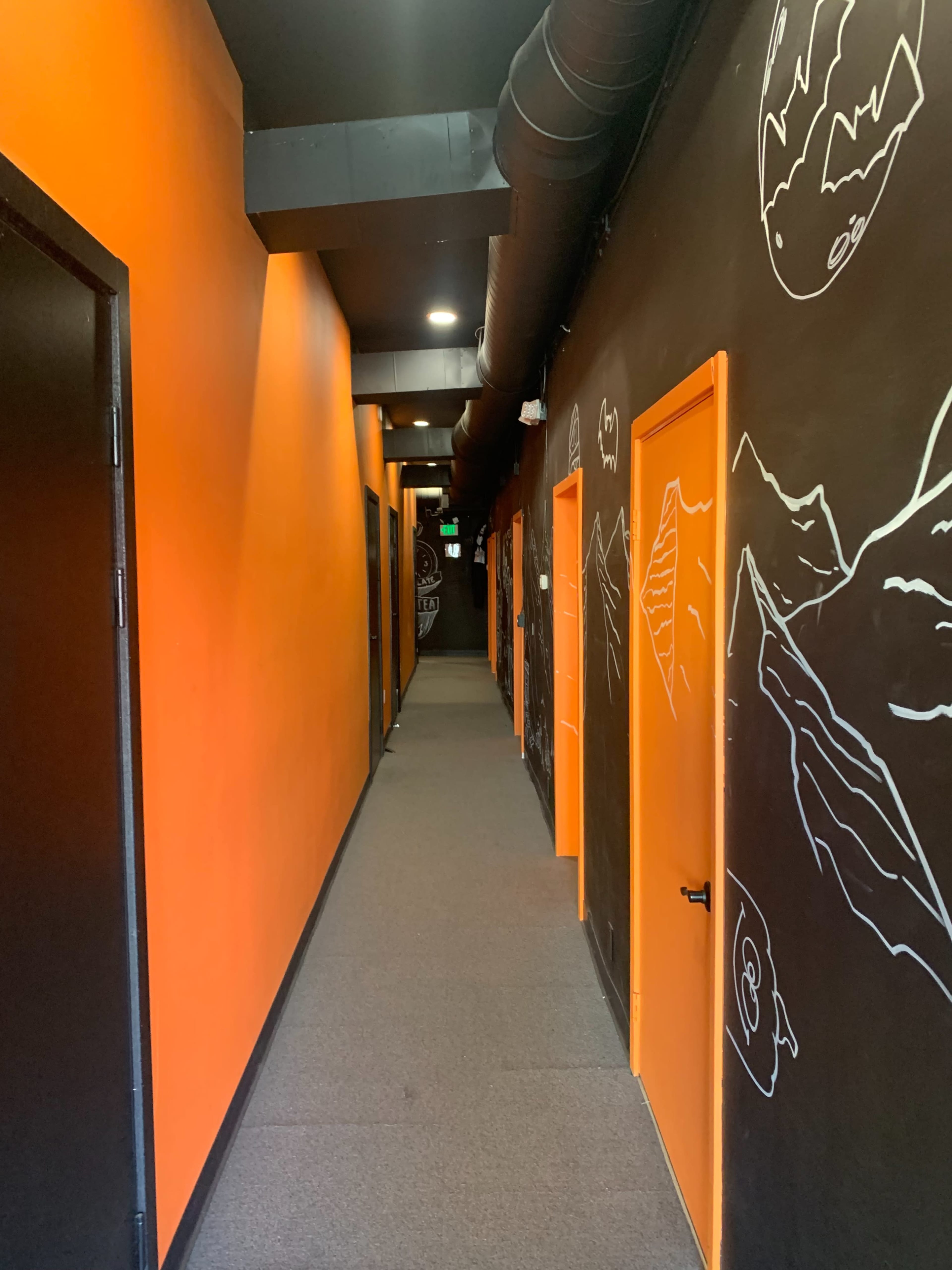 A narrow corridor with orange walls, black doors, and white sketches on the black wall.