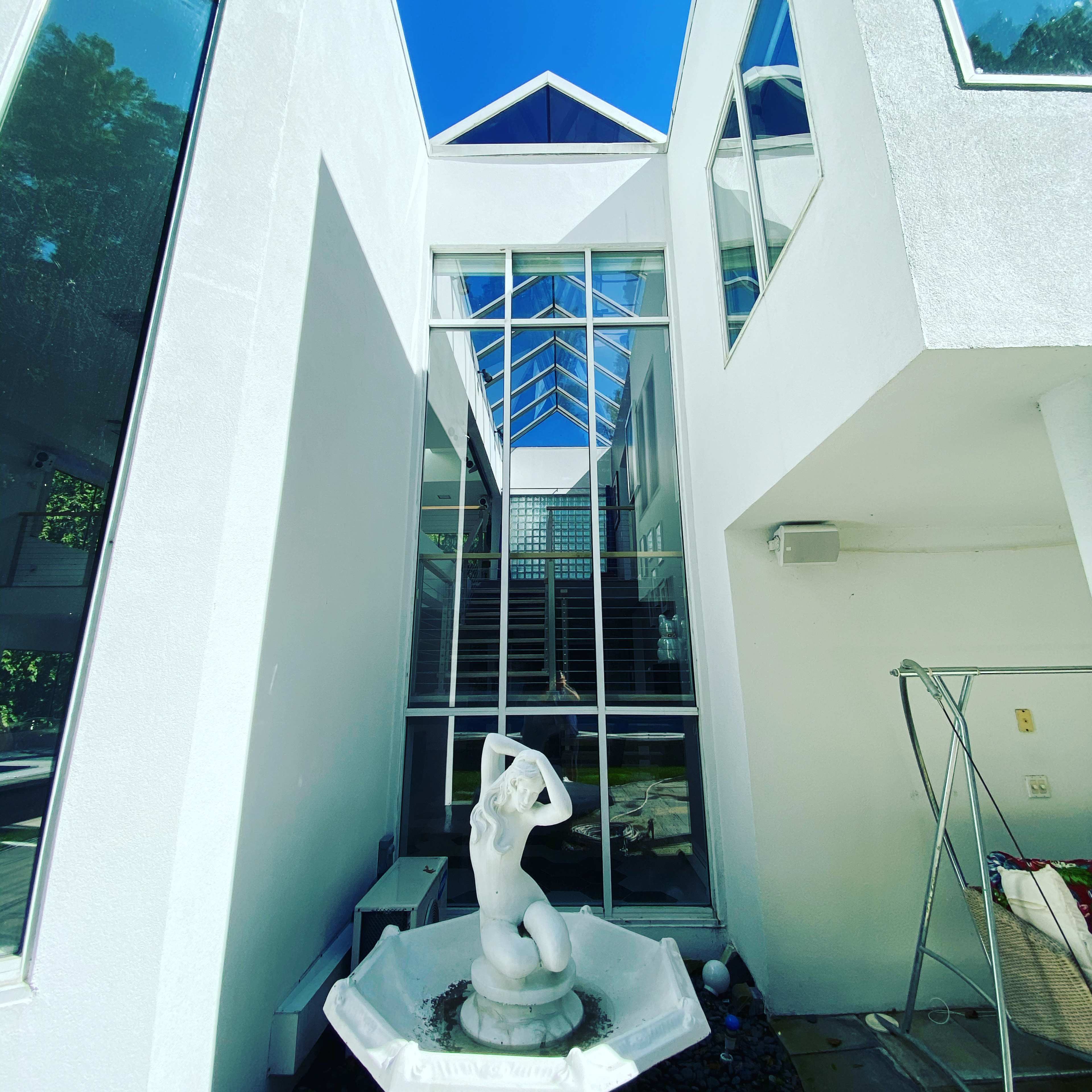 A modern architectural structure with large windows, featuring a white statue in a fountain at the center of an open courtyard.