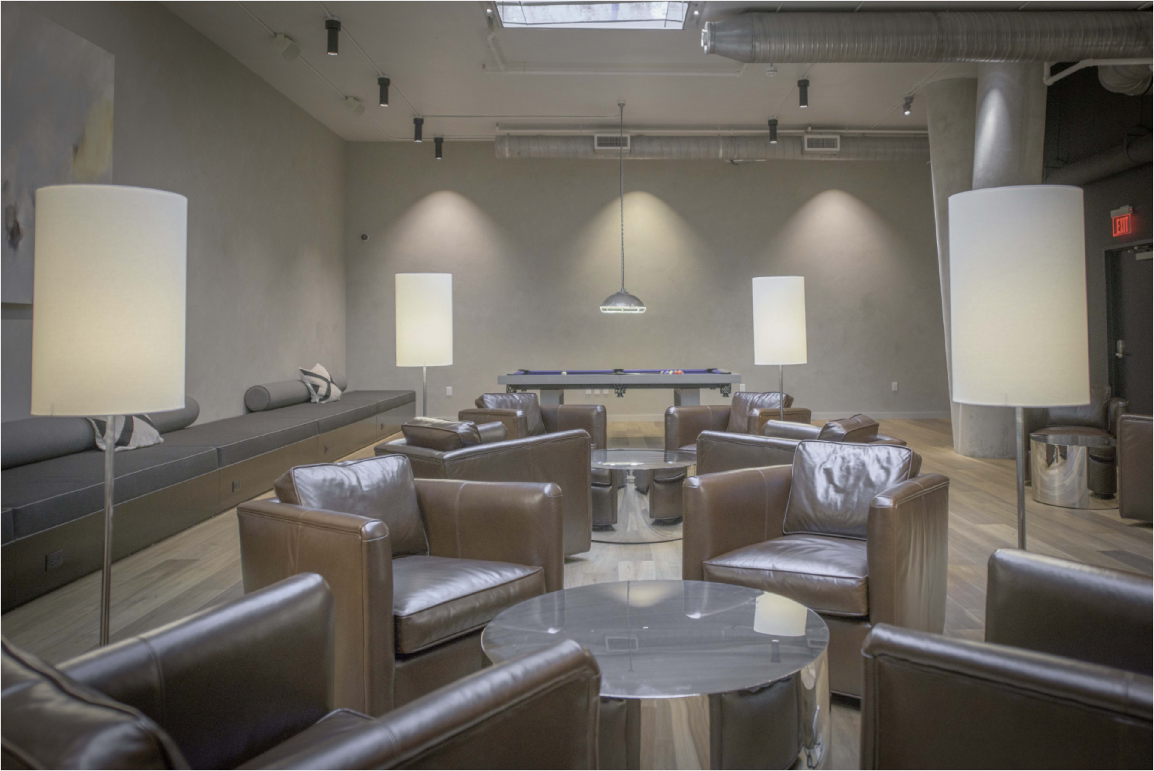 The image shows a modern lounge area with leather chairs, a glass table, and a pool table under a skylight.