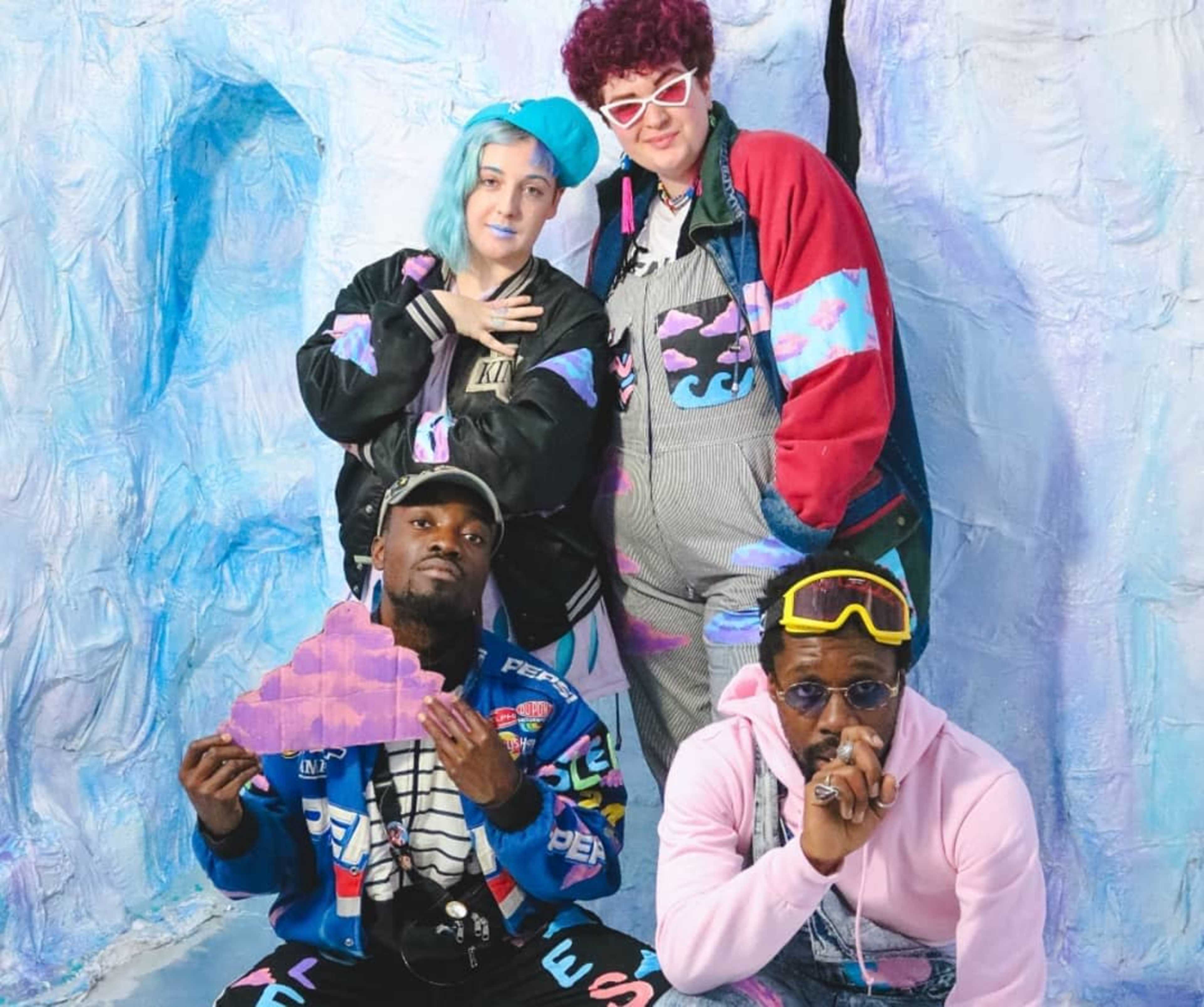 Four people pose together in a colorful, stylized setting with icy blue and purple backdrops.