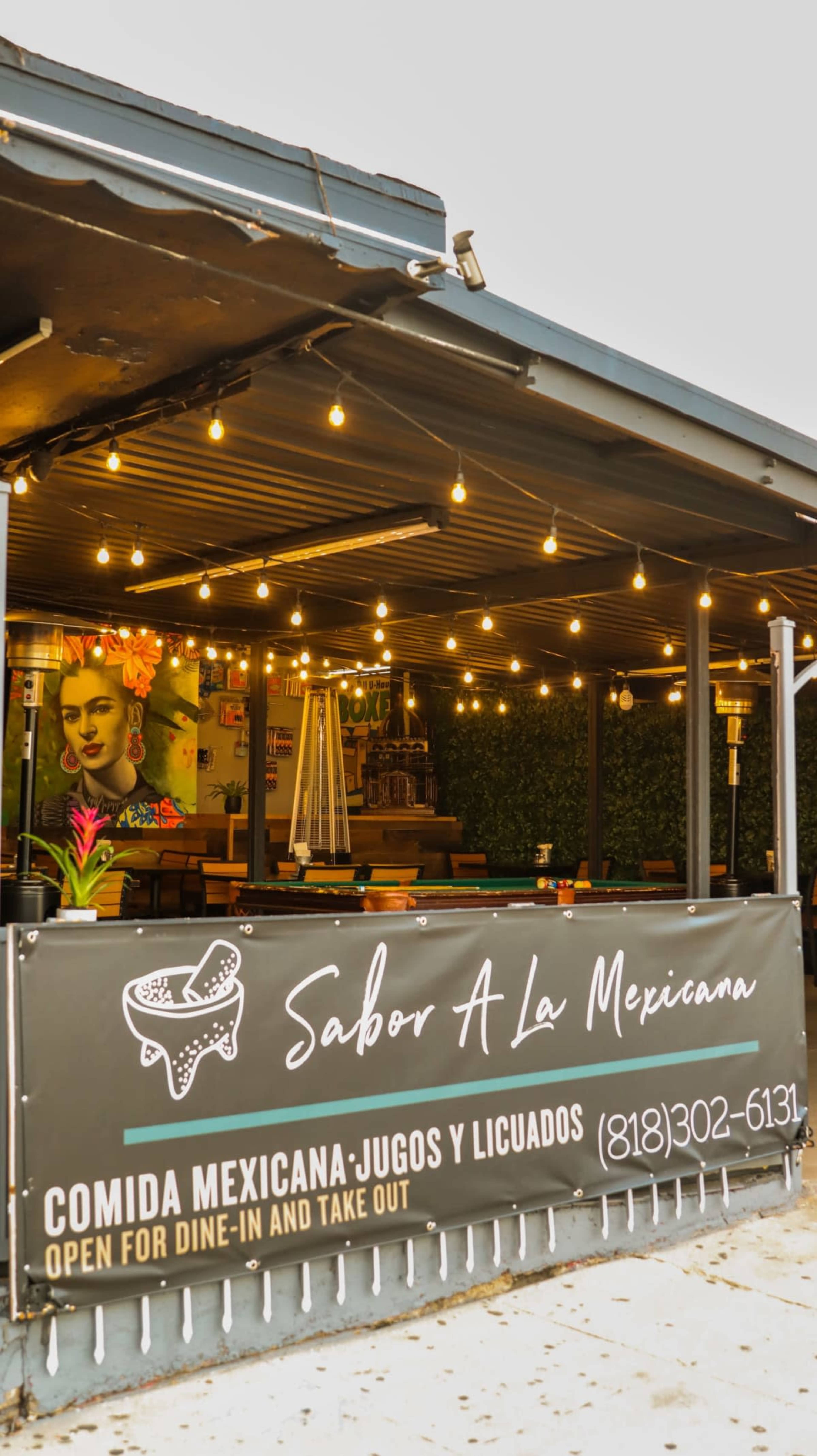 The image shows a Mexican restaurant's exterior with string lights and a sign that reads "Sabor A La Mexicana," featuring a vibrant mural of Frida Kahlo.
