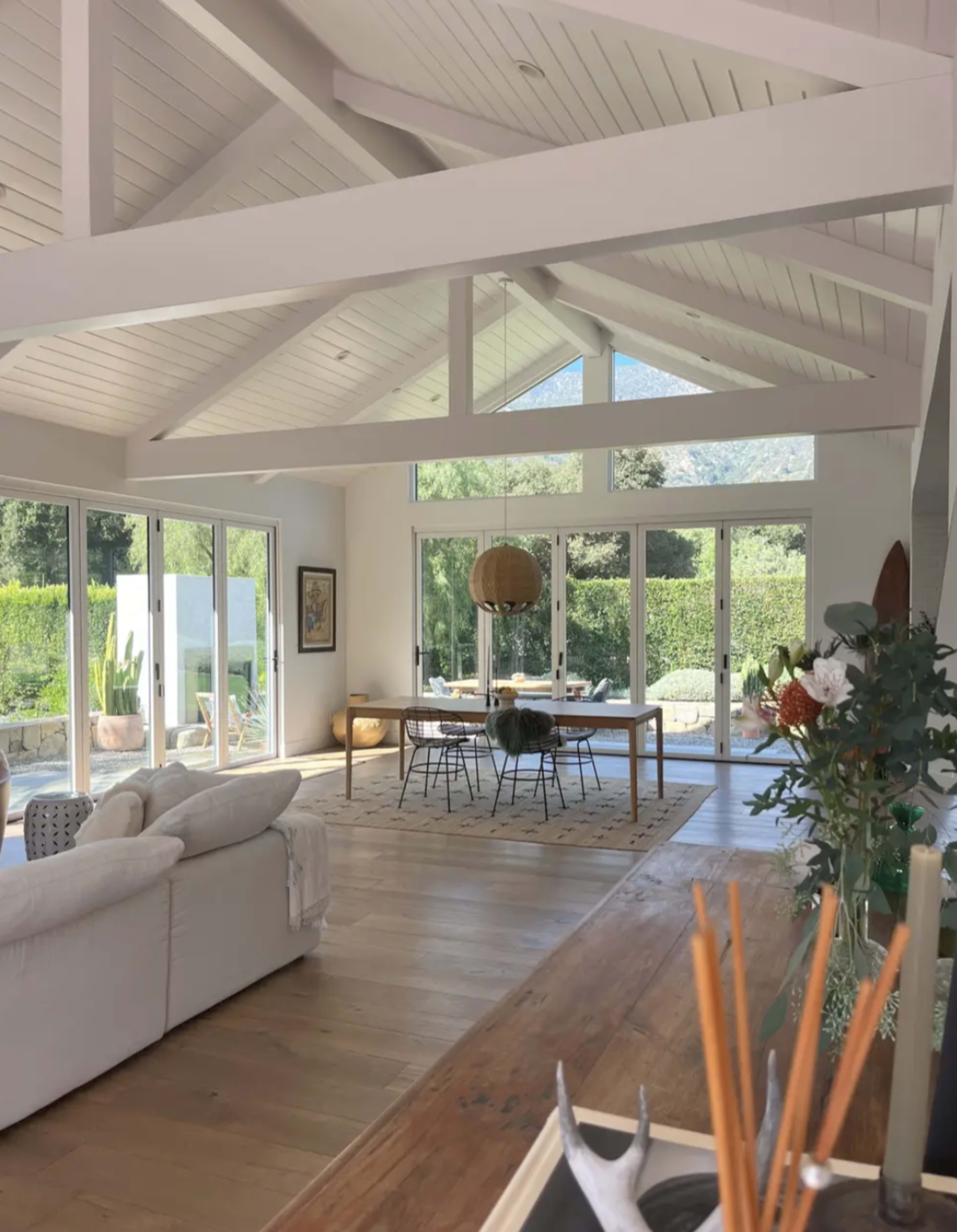 The image shows a spacious, modern living area with vaulted ceilings, large windows, and a dining table visible in the background.