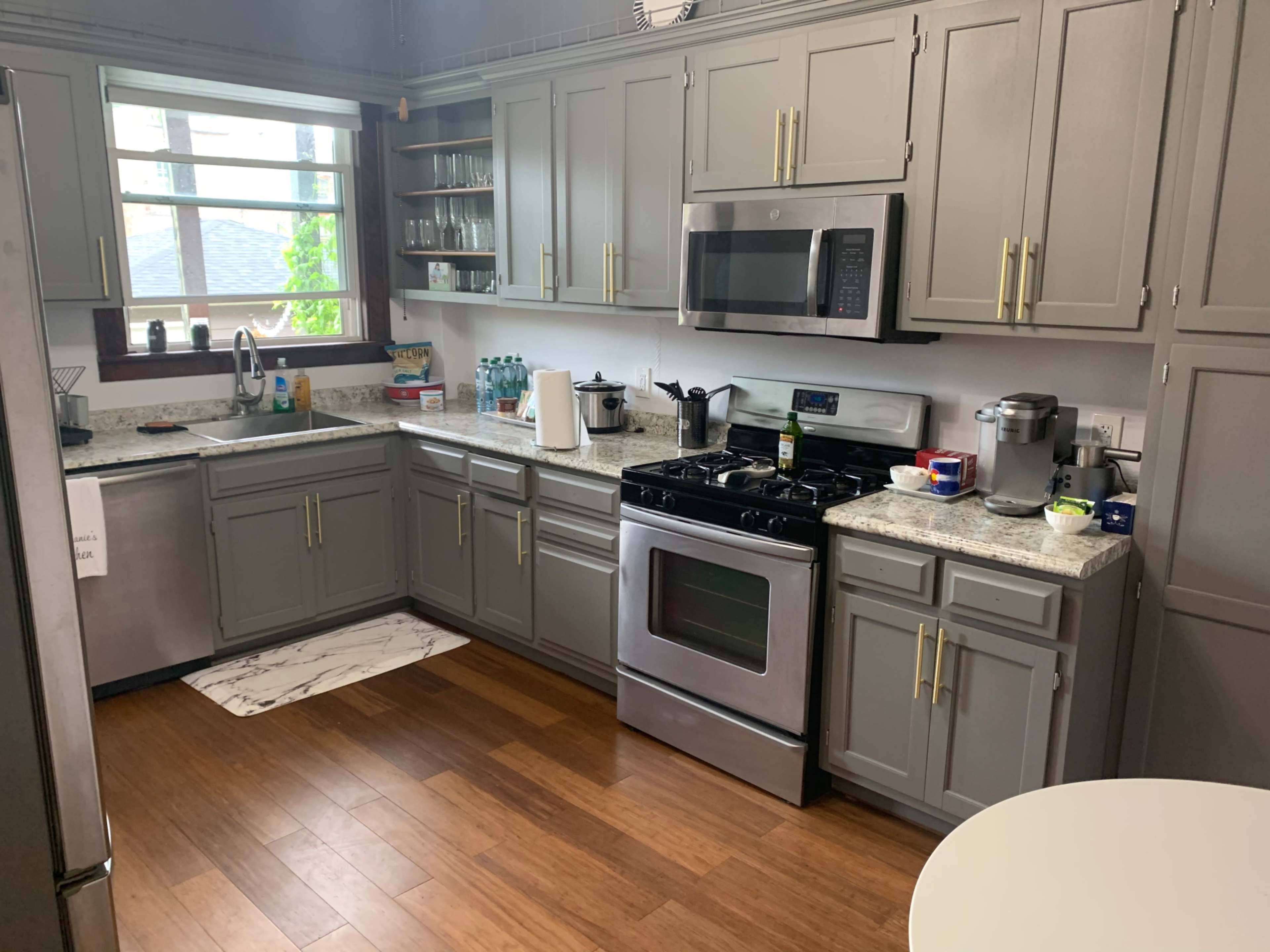 The kitchen features gray cabinets, a stainless steel refrigerator, a gas stove, and a countertop with various kitchen appliances and utensils.