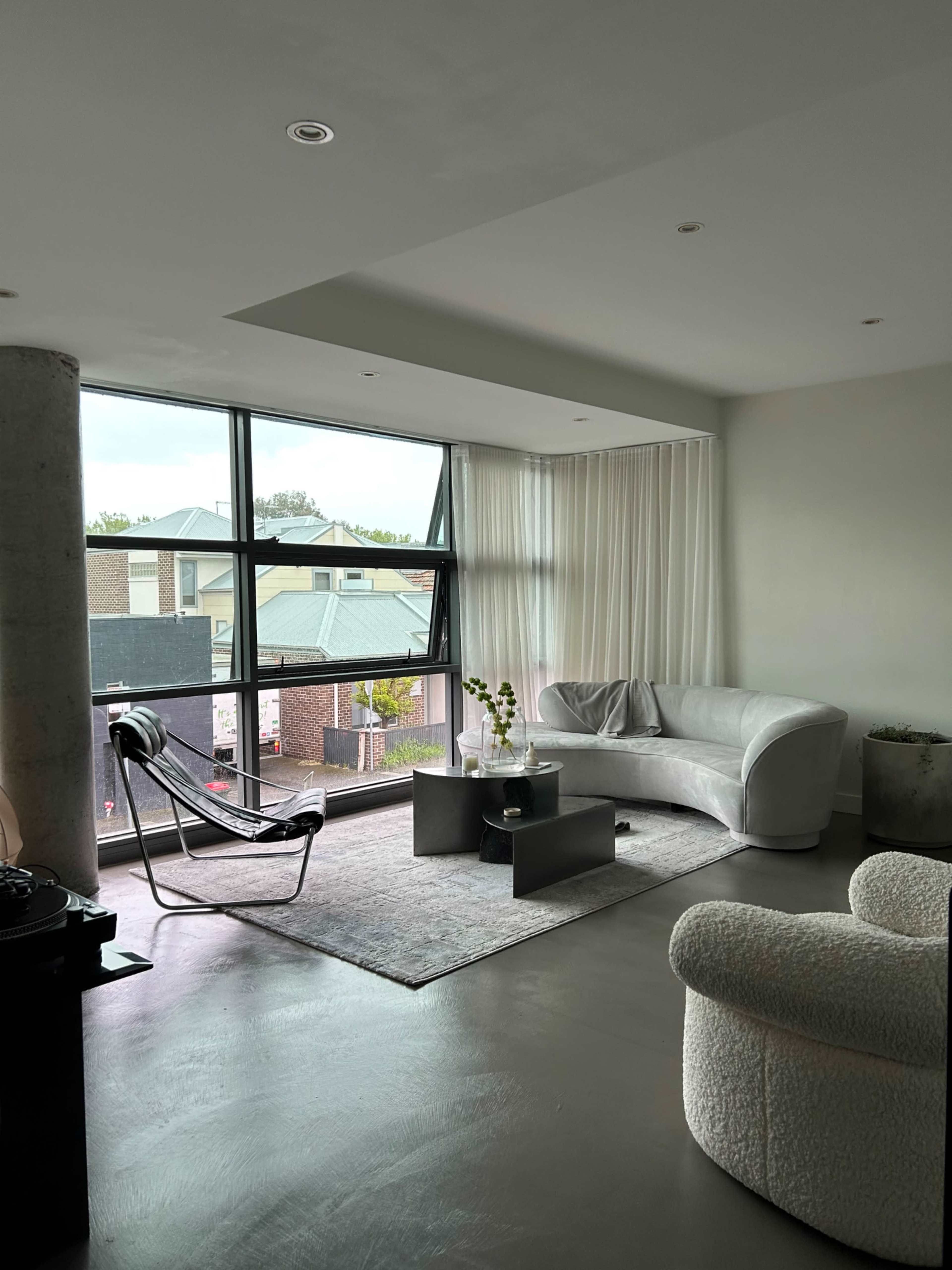 A modern living room with a large window, light-colored furniture, and a minimalist decor style.