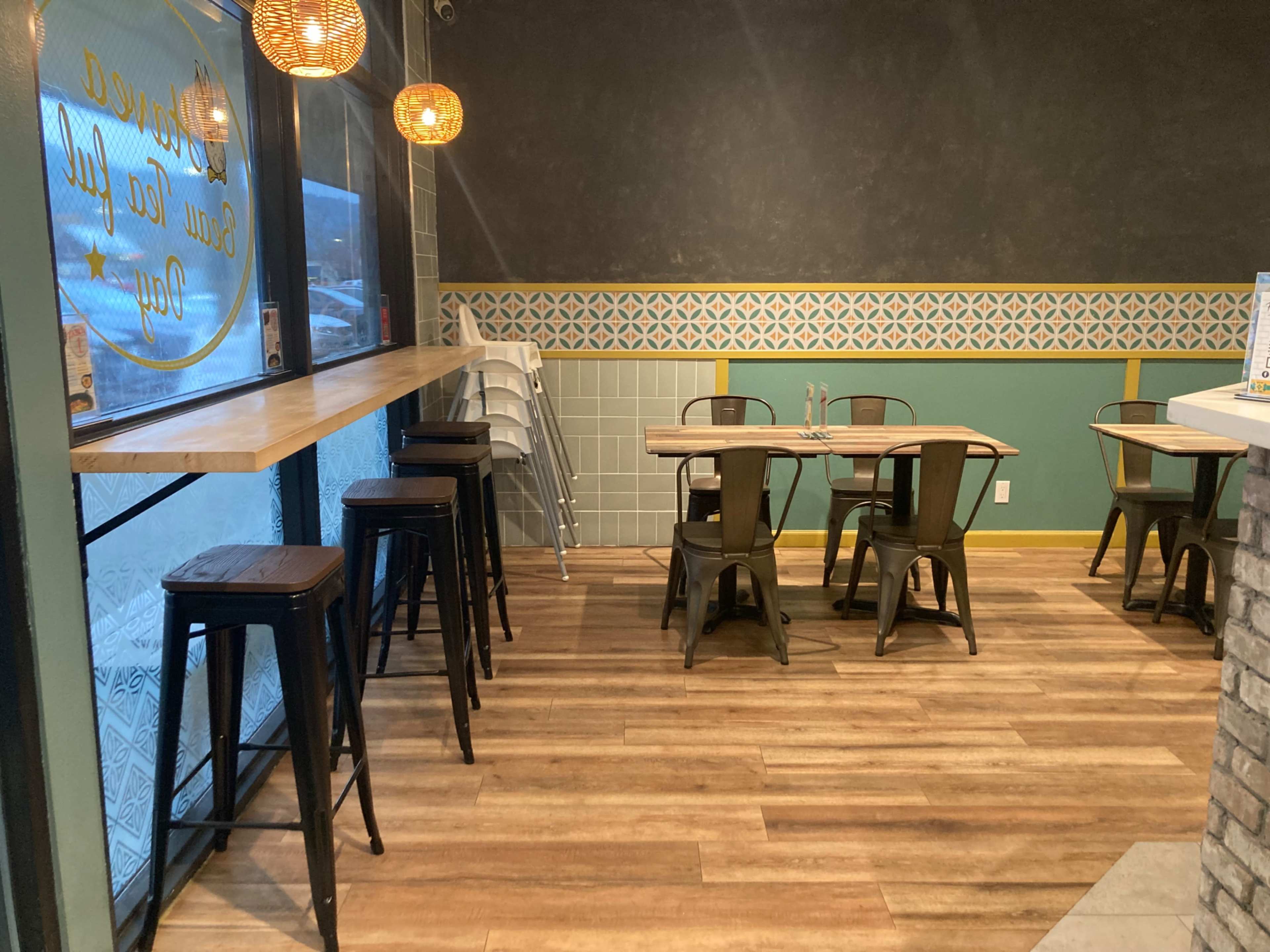 A cozy restaurant interior with wooden tables, metal chairs, and pendant lights hanging above.
