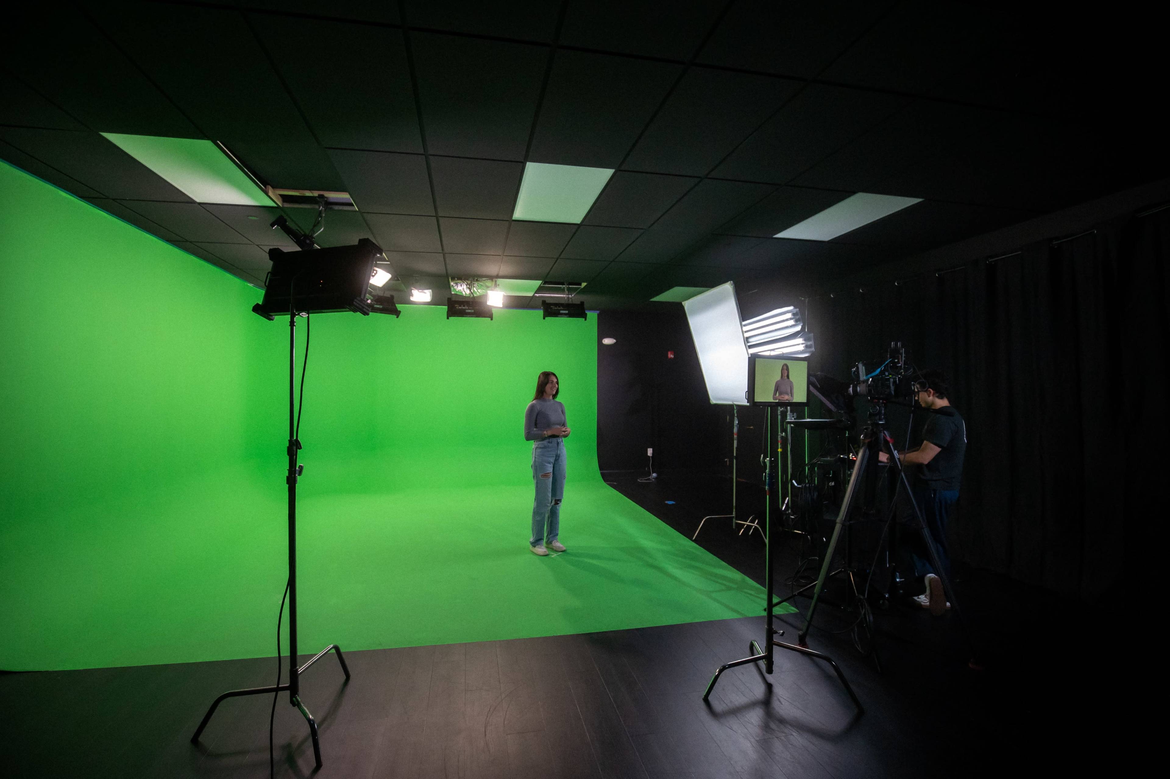 A person stands on a green screen stage with studio lights and cameras set up around them.