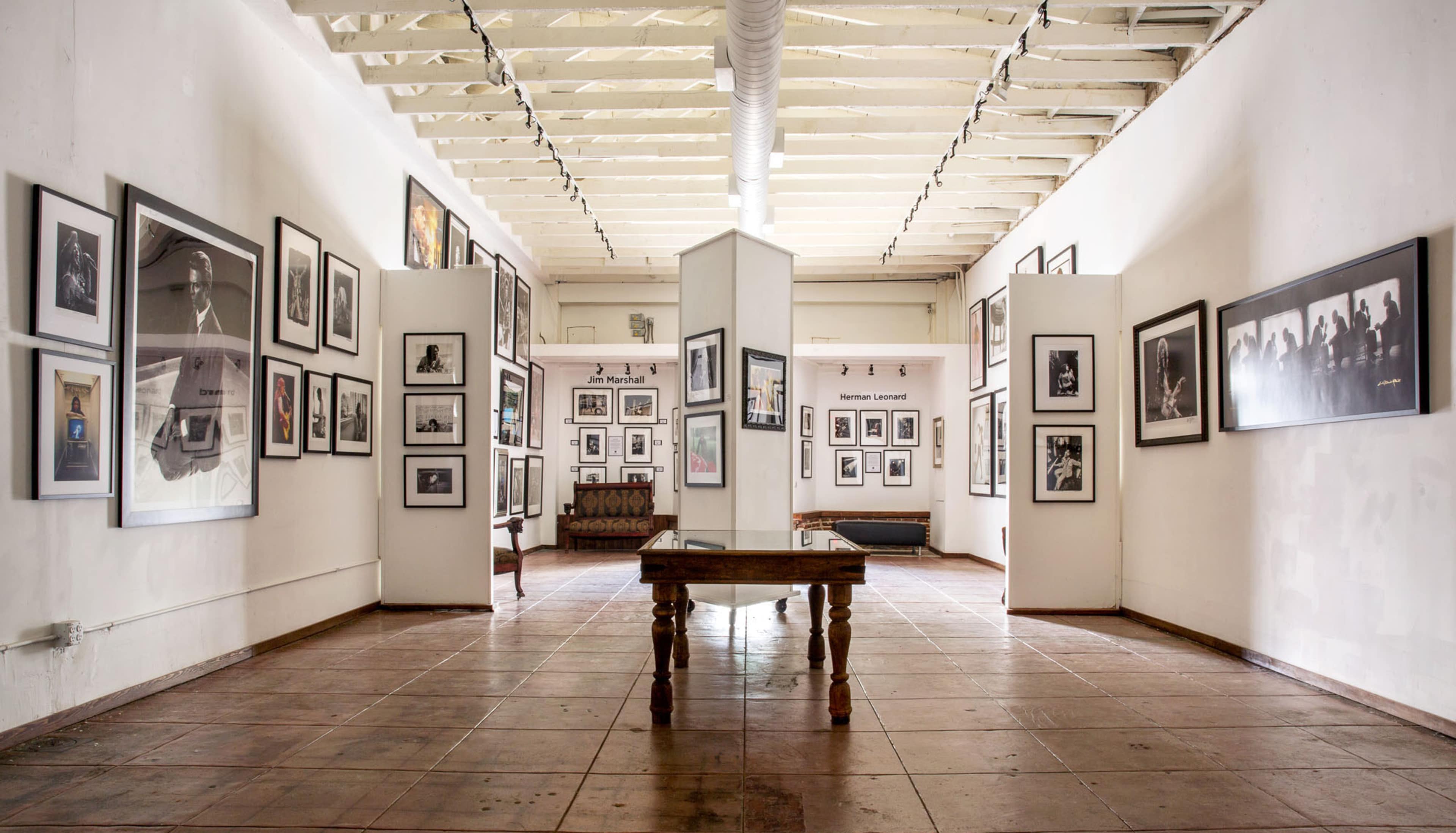 An art gallery with framed photographs displayed on the walls and a wooden table in the center.