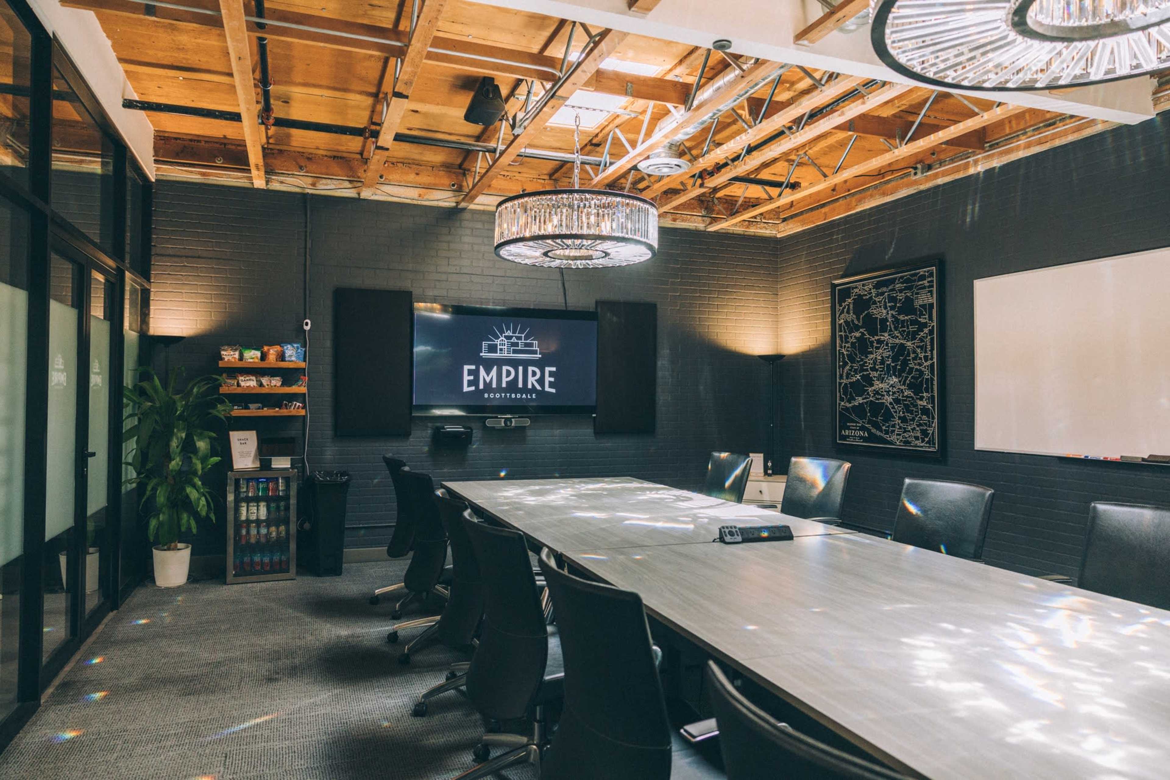 The image shows a modern conference room with a long table, black chairs, and a large screen displaying the word "EMPIRE," set against a backdrop of exposed wooden beams and decorative lighting.