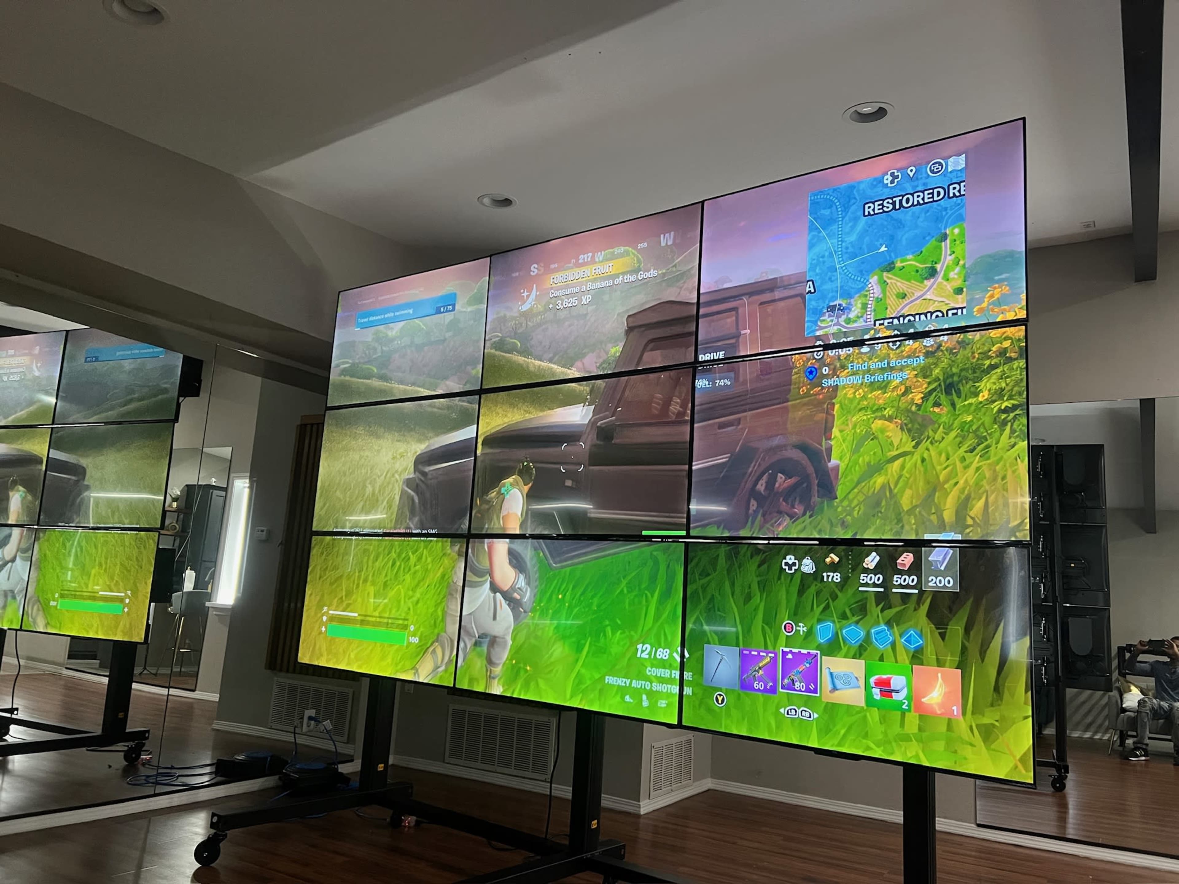 A large video wall displays a game interface featuring a character in a vibrant landscape.