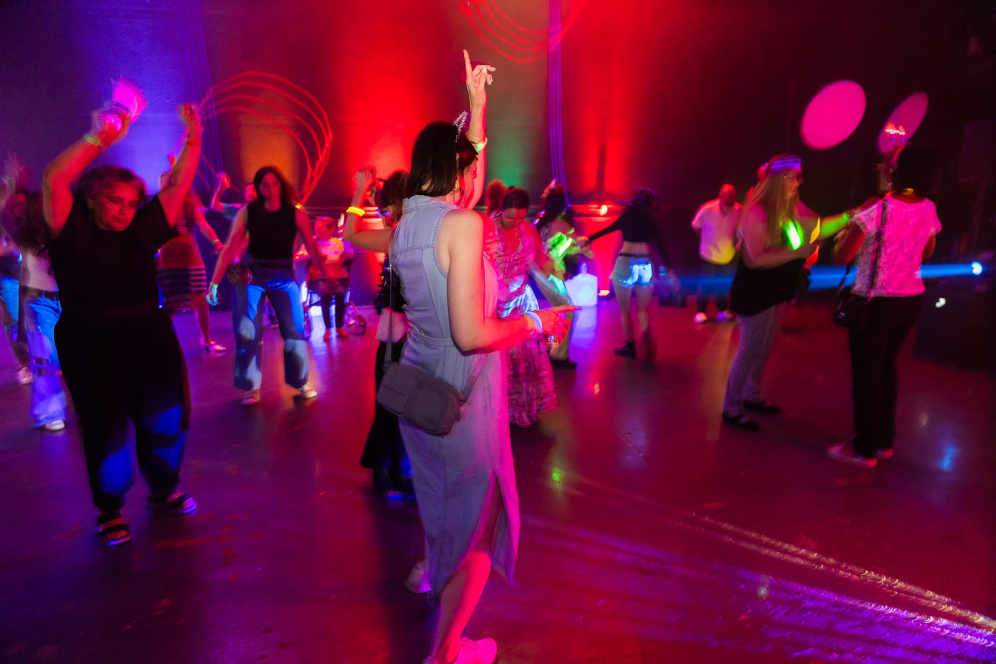 A group of people is dancing in a dimly lit venue with colorful lights illuminating the scene.