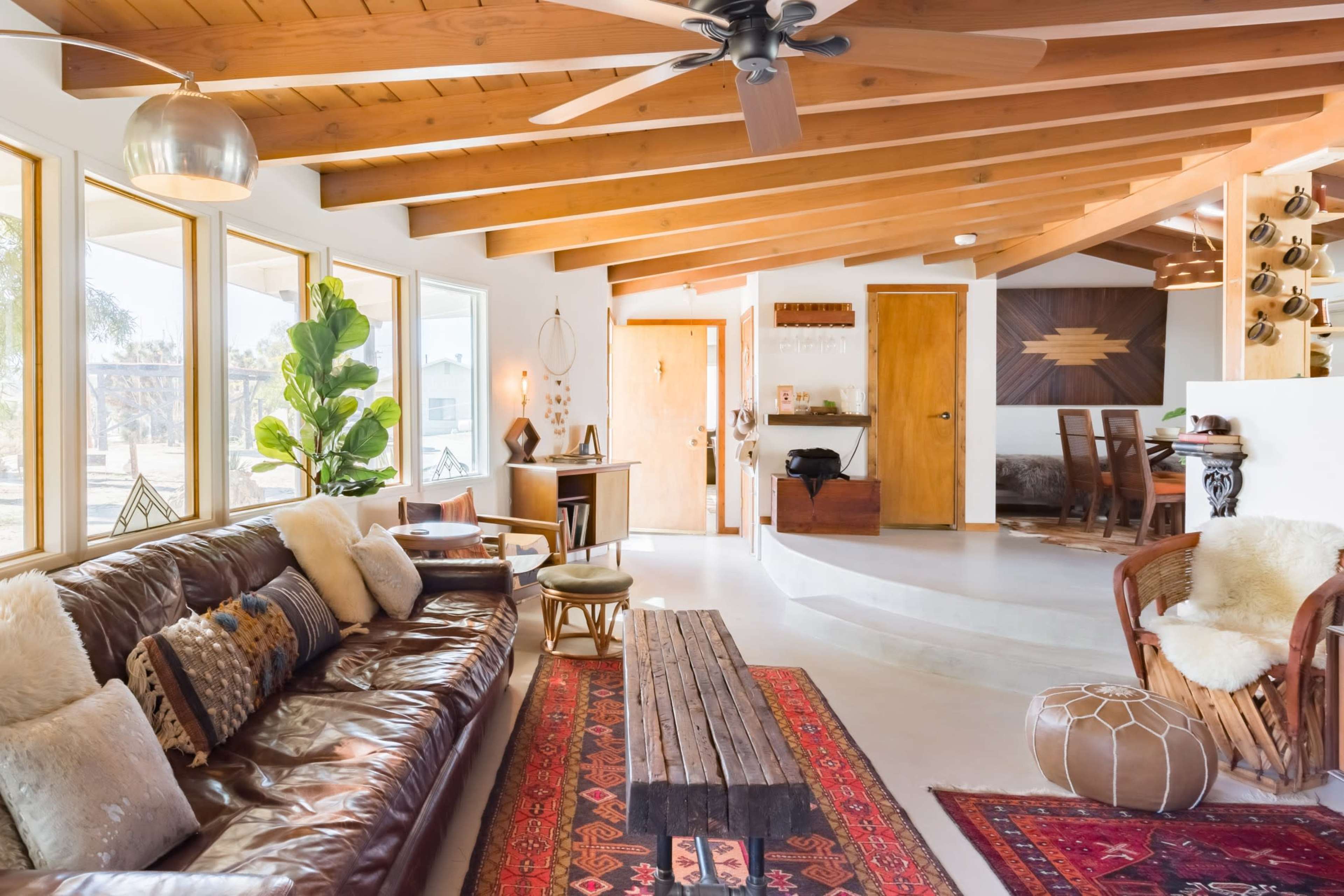 A bright living room features a leather sofa, a wooden coffee table, and large windows, with a mix of rustic and modern decor.