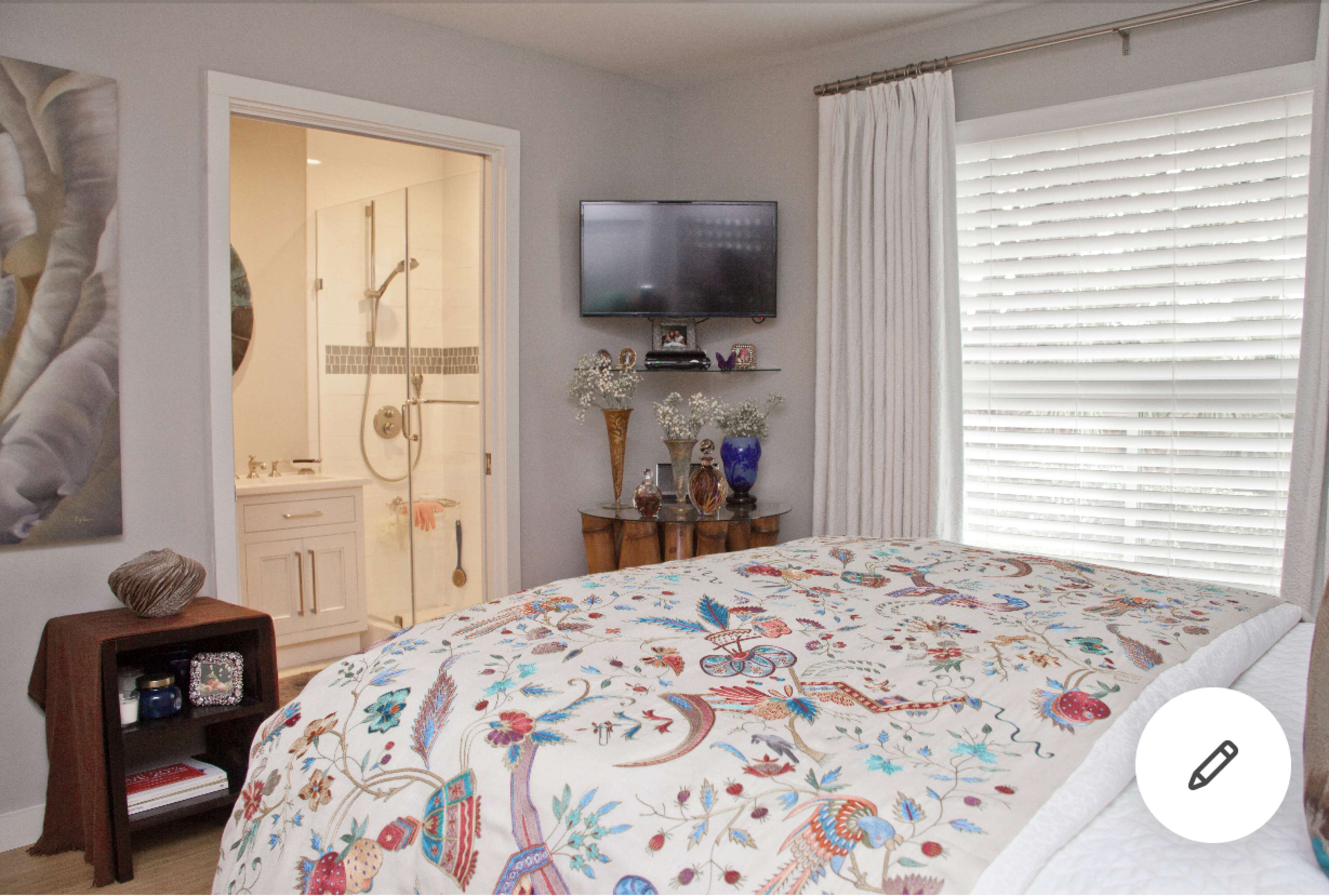 A cozy bedroom with a colorful, patterned bedspread, a small wooden nightstand, and a bathroom visible through an open door.