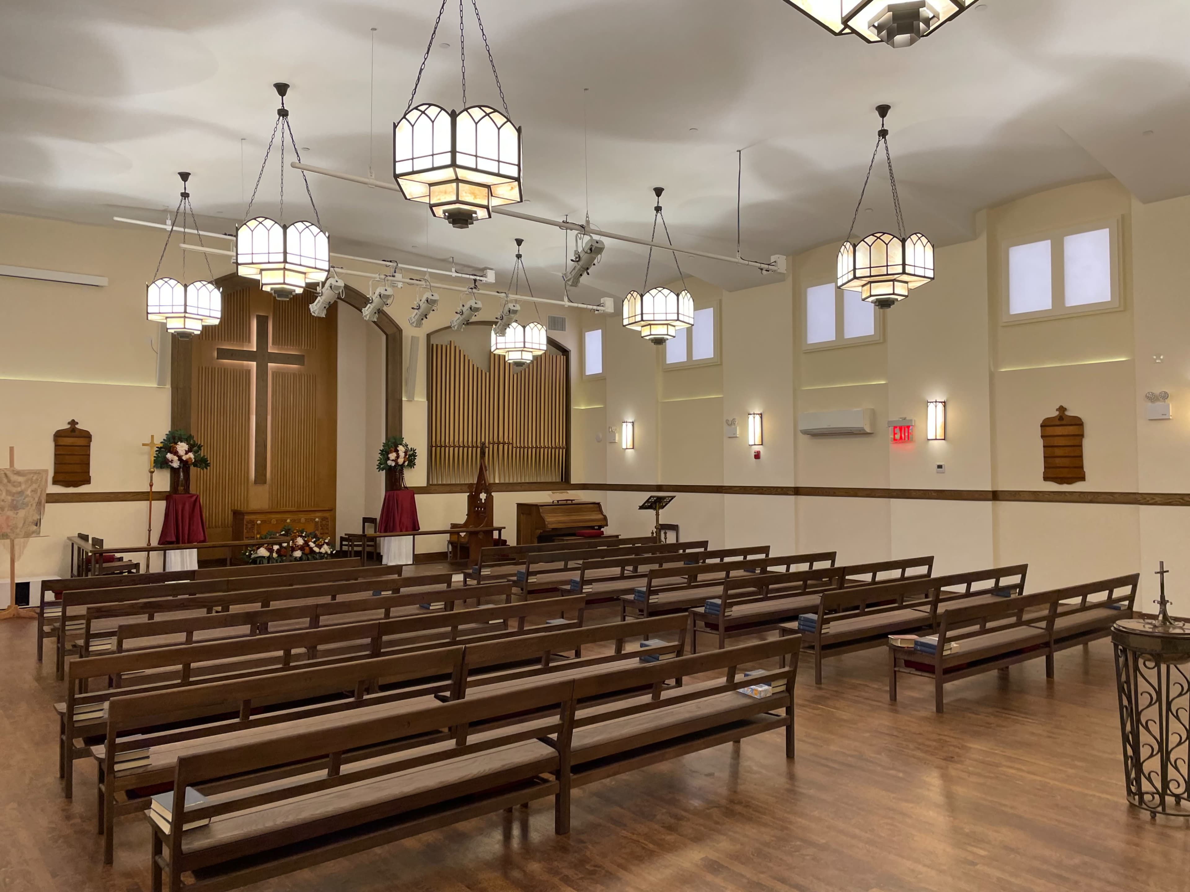 A spacious church interior with wooden pews arranged facing a front stage that has a large cross and an organ.