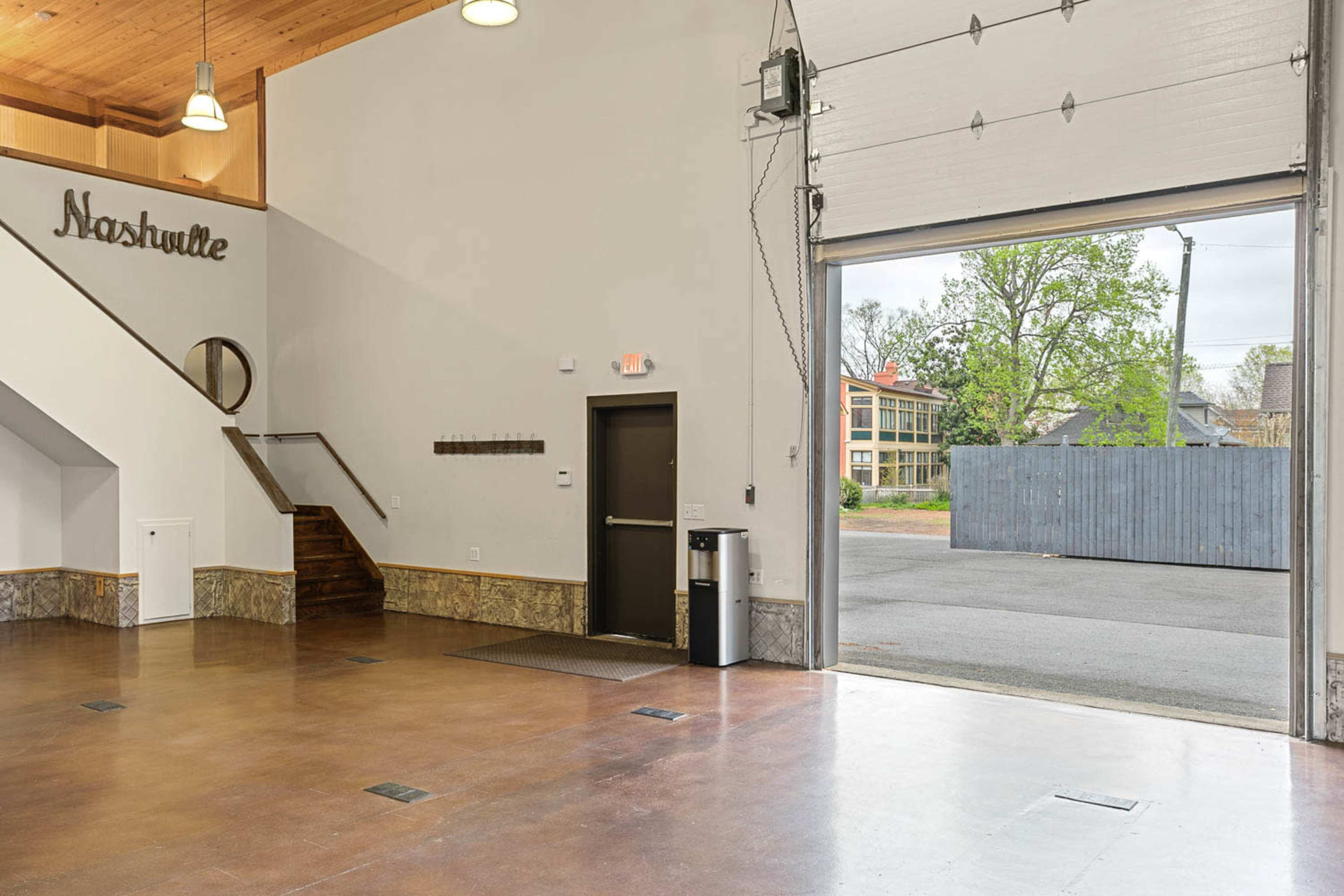 The image shows an empty interior space with a staircase on the left, a door leading outside, and a sign that reads "Nashville" on the wall.