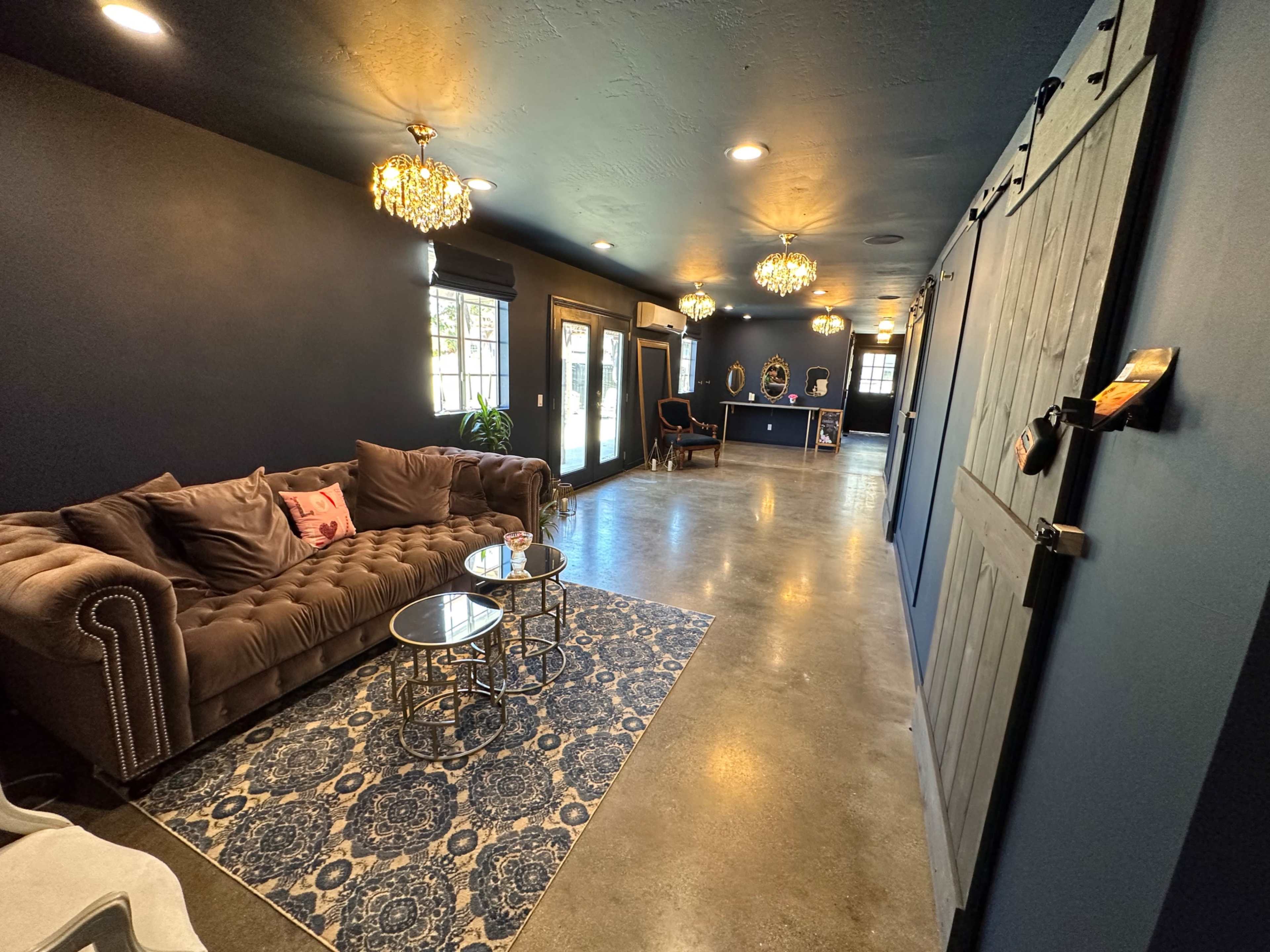 A cozy interior space with a velvet sofa, decorative lighting, and a patterned rug, leading to a counter area at the end.