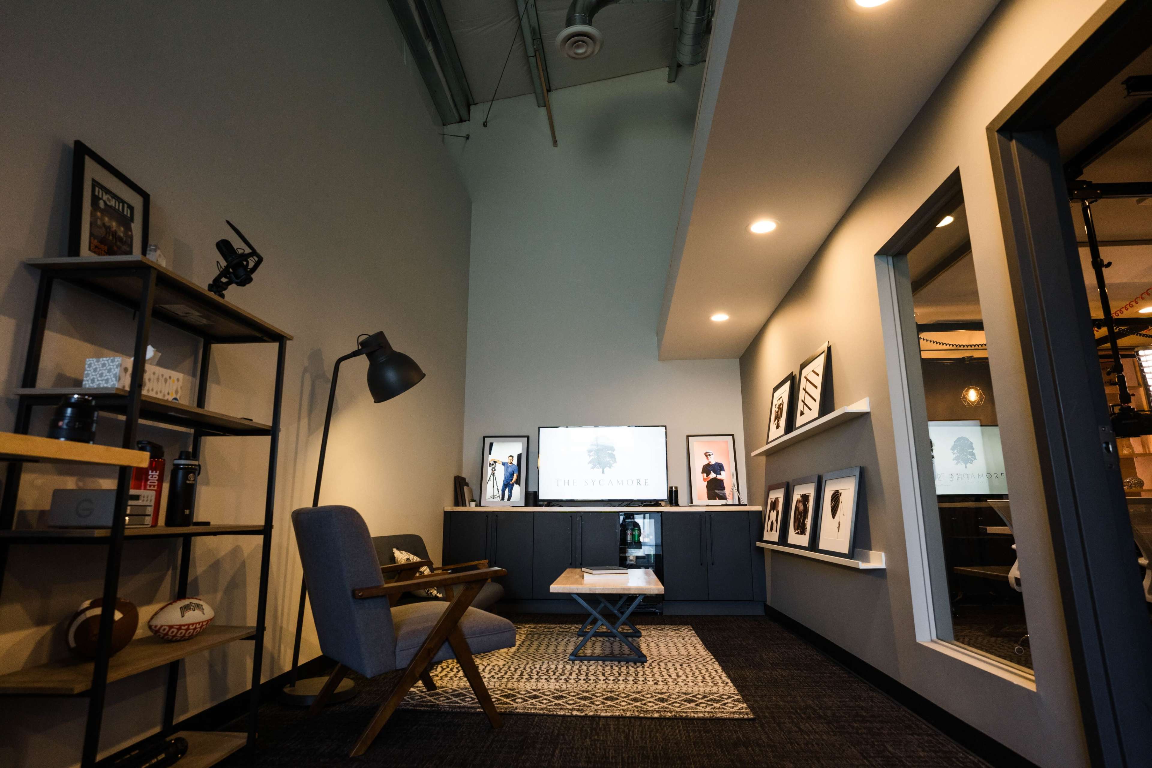 A modern office space with a decorative shelving unit, a gray armchair, a coffee table, and a television displaying a logo on the wall.