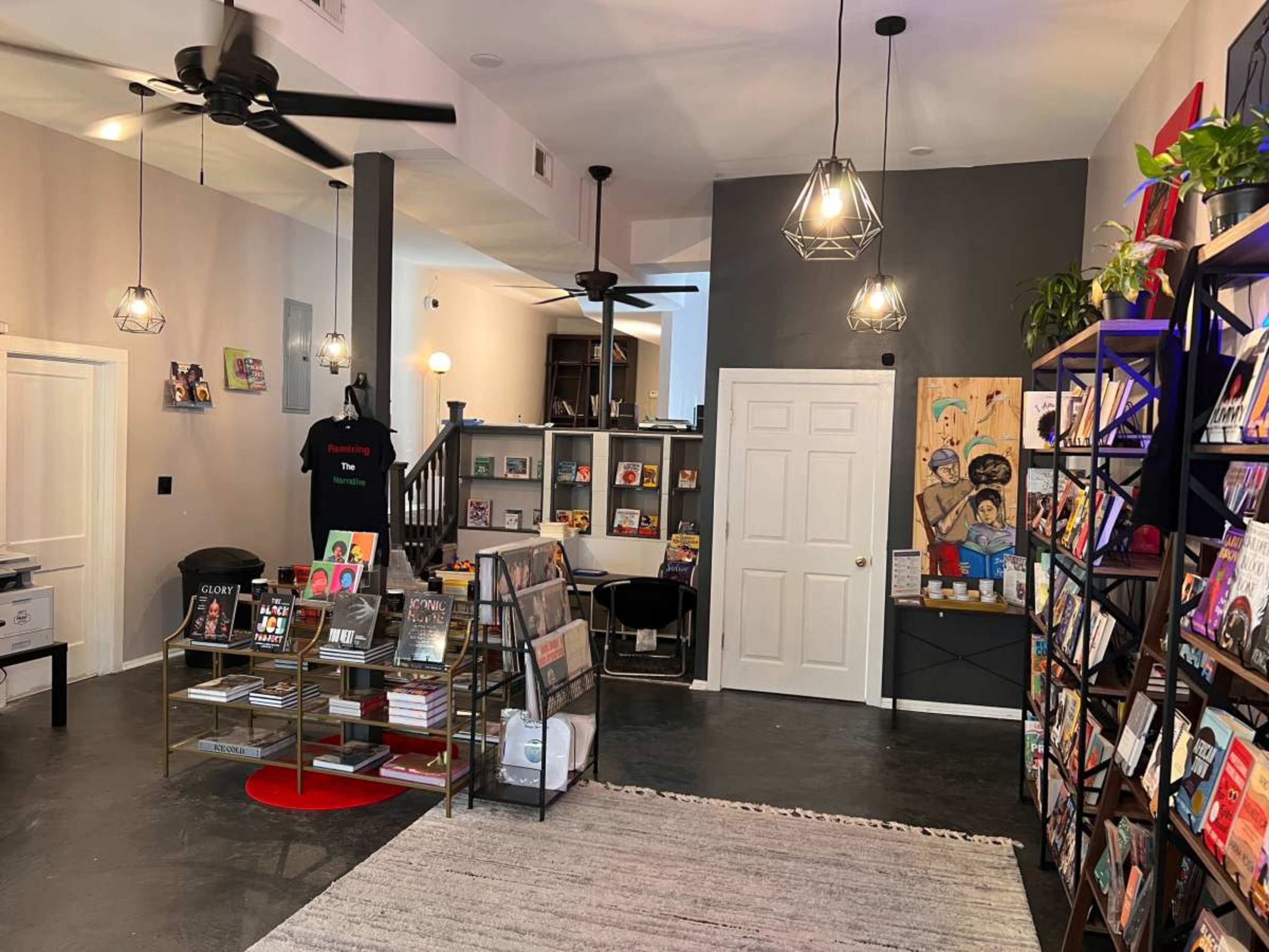 The image shows a modern retail space featuring bookshelves filled with magazines and books, seating areas, and decorative lighting.