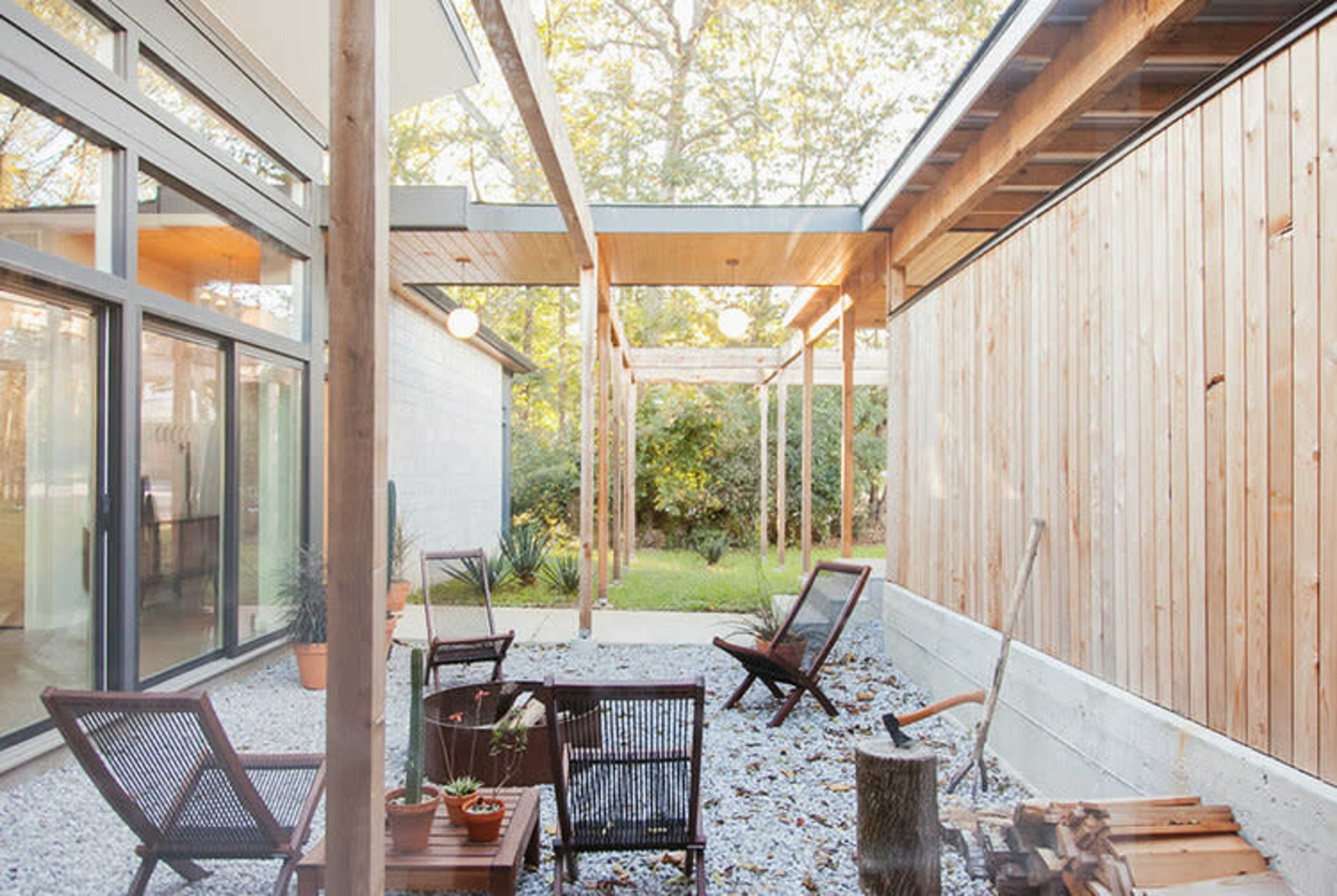 A modern interior space with large windows, a wooden wall, and a seating area surrounded by greenery outside.