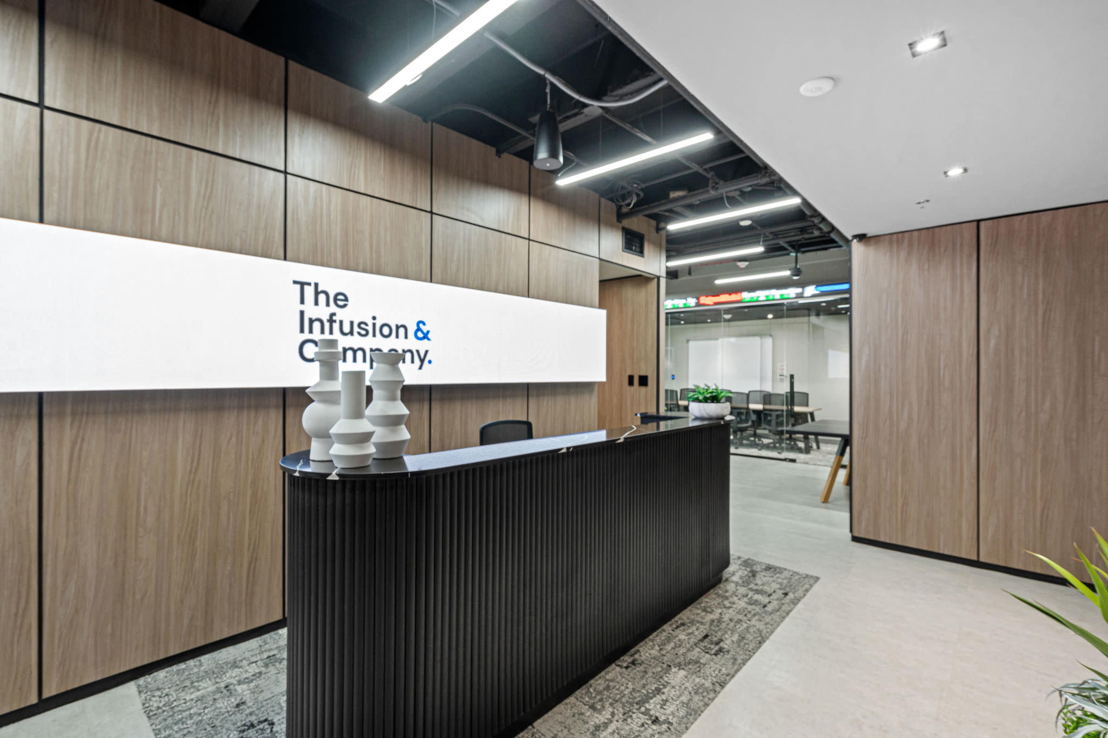 The image shows a modern reception area with a dark reception desk, a large backlit sign displaying the company name, and wooden paneling on the walls.