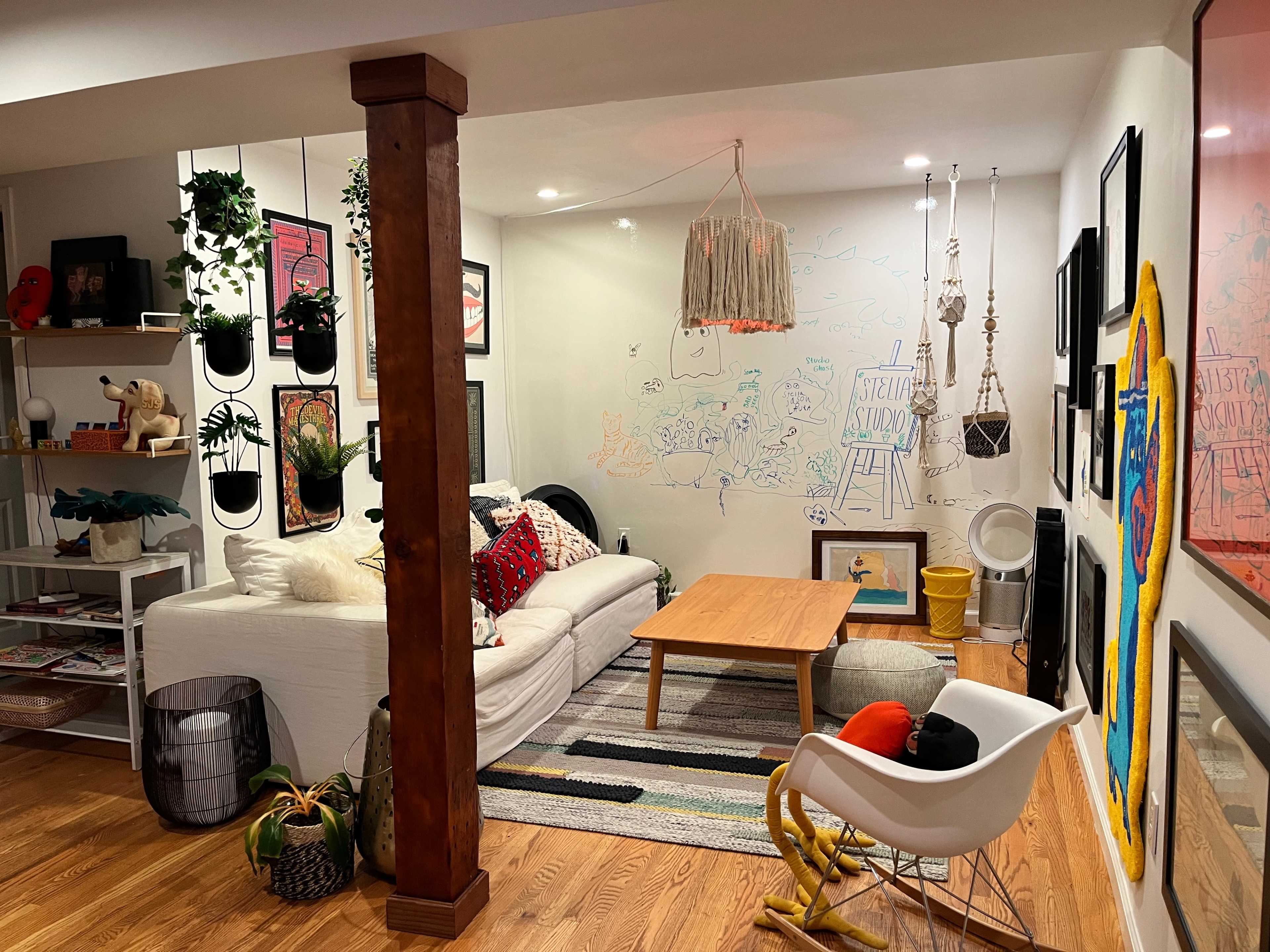 A cozy living space with a white couch, a wooden coffee table, and colorful decor on the walls, including plants and various artistic elements.